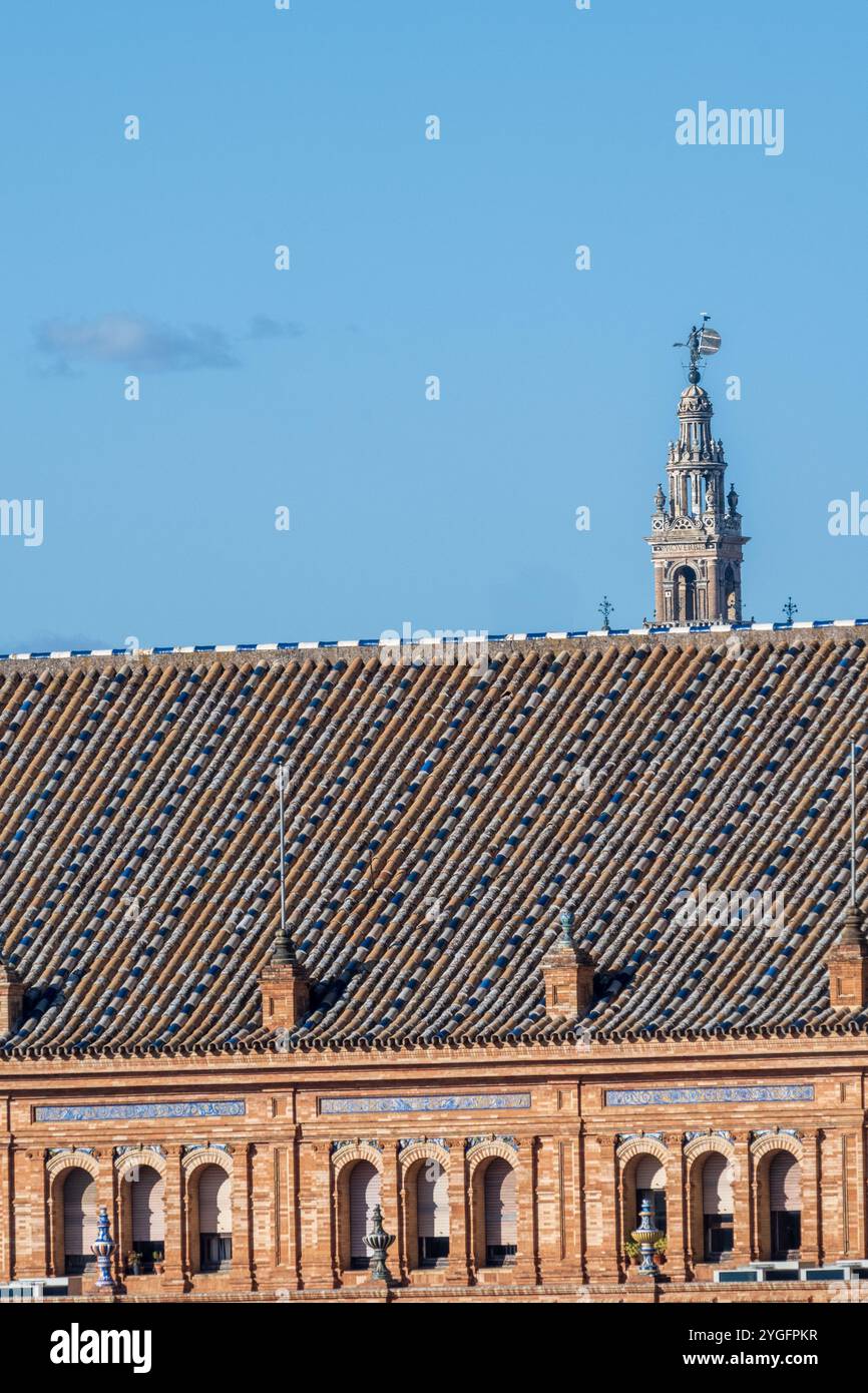 Ein lebhafter Blick auf die Skyline des Turms La Giralda, der hinter einem historischen Dach in Sevilla, Spanien, ragt. Hellblauer Himmel ergänzt die architektonische Deta Stockfoto