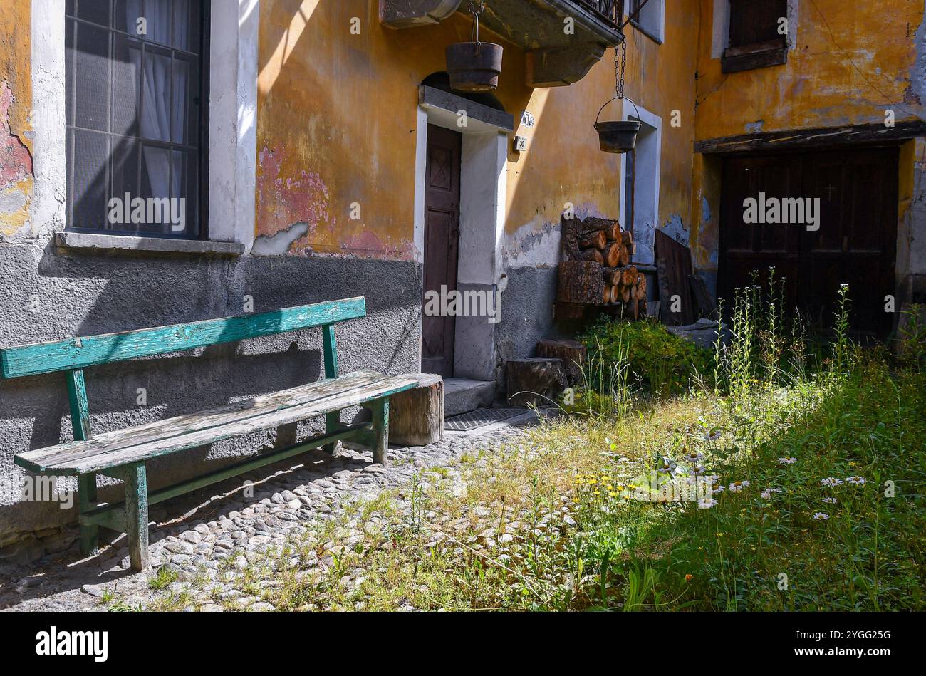 Kopfsteinpflasterhof eines alten Berghauses mit Holzbank und Holzschuppen im Alpendorf Dolonne, Courmayeur, Aostatal, Italien Stockfoto