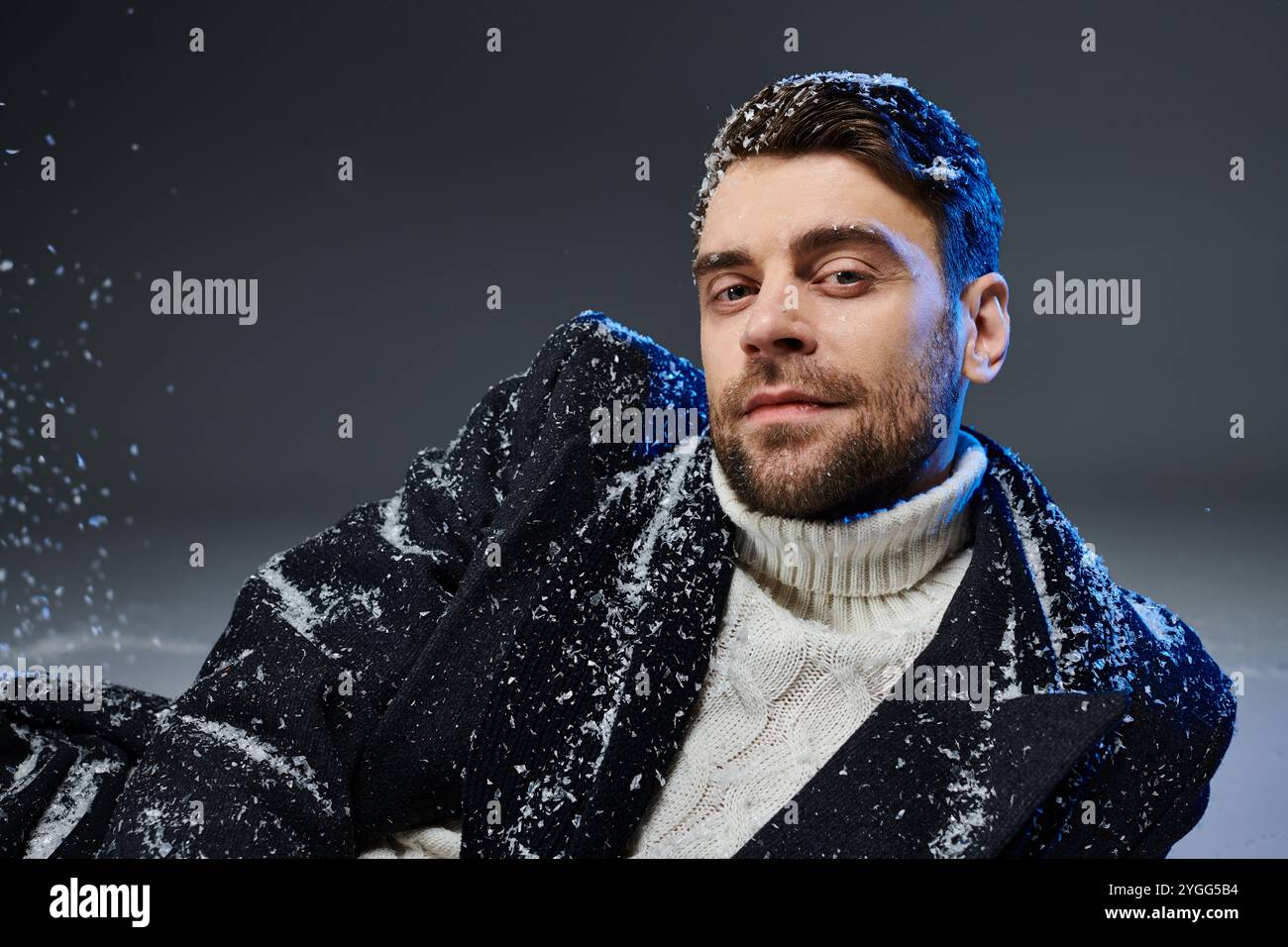 Ein selbstbewusster junger Mann entspannt sich in einer verschneiten Kulisse und strahlt Charme und Wärme in Winterkleidung aus Stockfoto