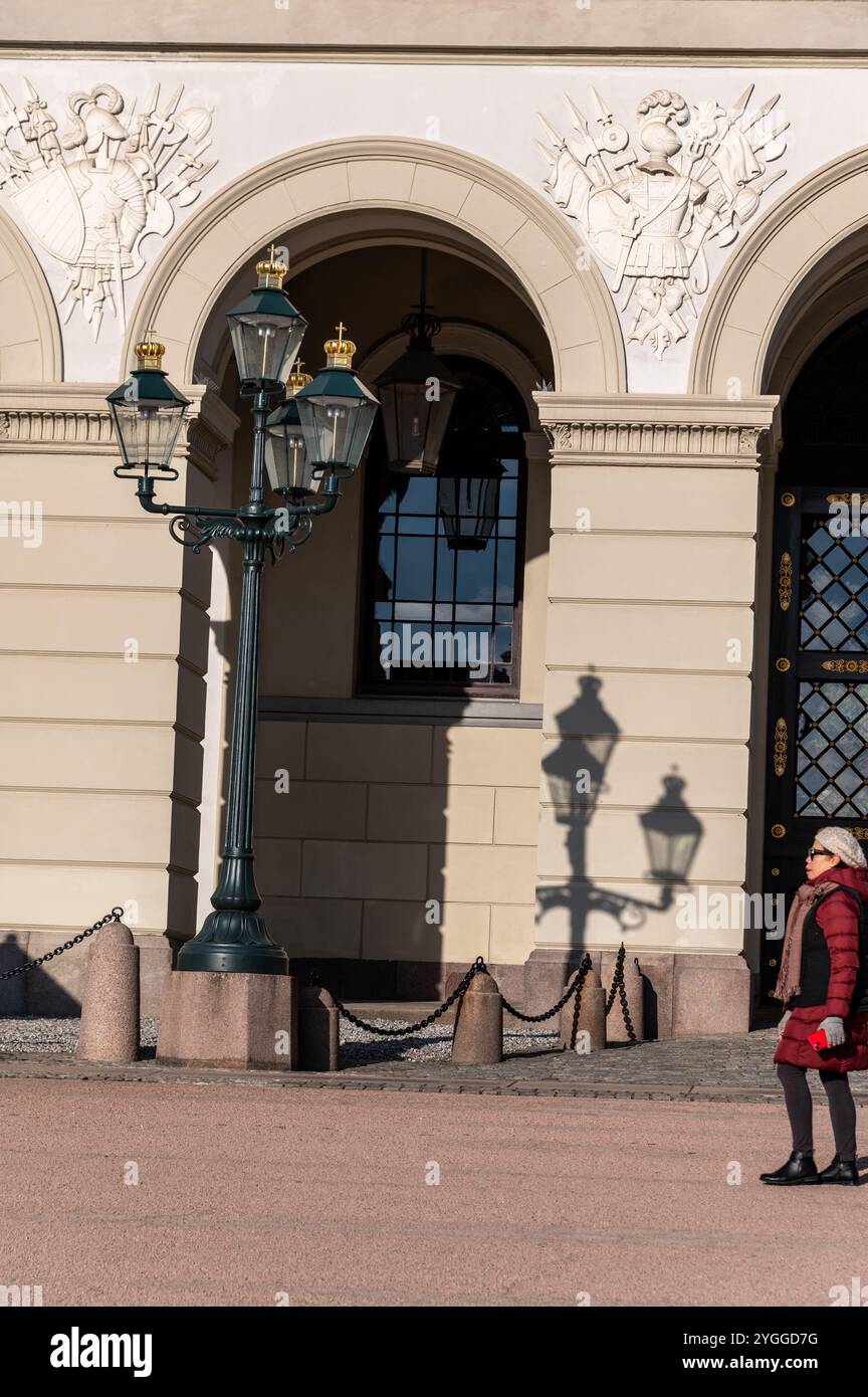 Ein Tourist, der an einem alten Straßenlaternenpfosten vorbeikommt, der seinen Schatten auf die Wand des Königspalastes wirft, der offiziellen Residenz des heutigen Norwegers Stockfoto