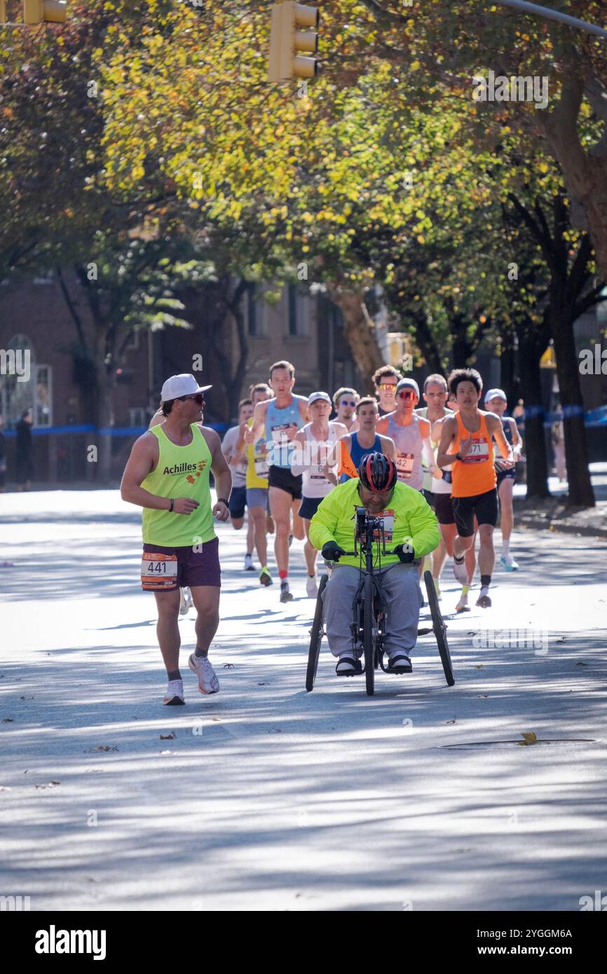 Beim NY-Marathon 2024 war eine Elite-Gruppe von Läufern hinter einem Rollstuhlsportler mit seinem Achilles International Guide. An der 16-km-Marke in Brooklyn. Stockfoto