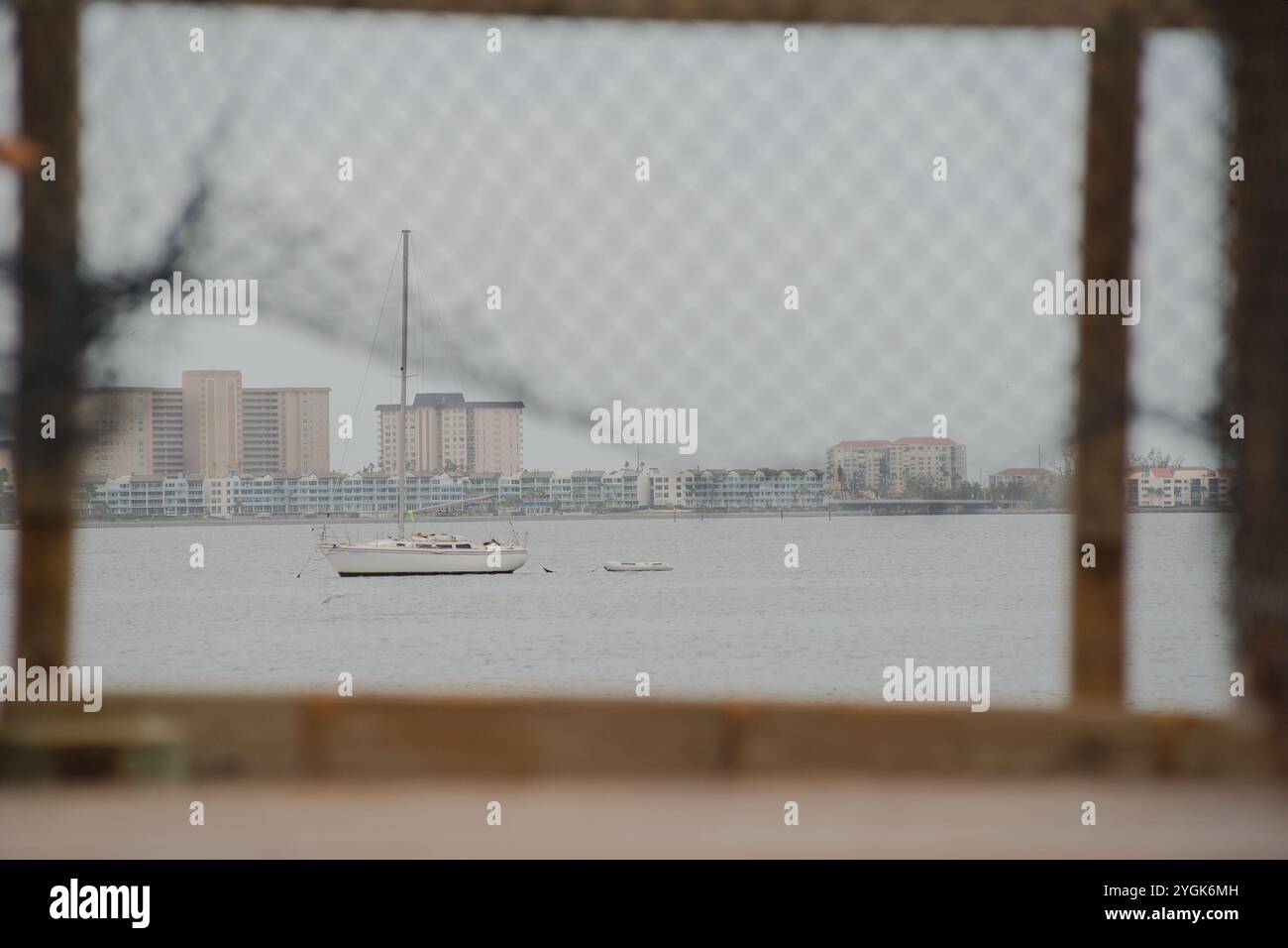 POV-führende Linien, Blick durch Maschendrahtzaun auf beschädigtem Holzsteg. Blick auf ein Segelboot in Boca Ciega Bay Gulfport Florida Beach. Nach St Stockfoto