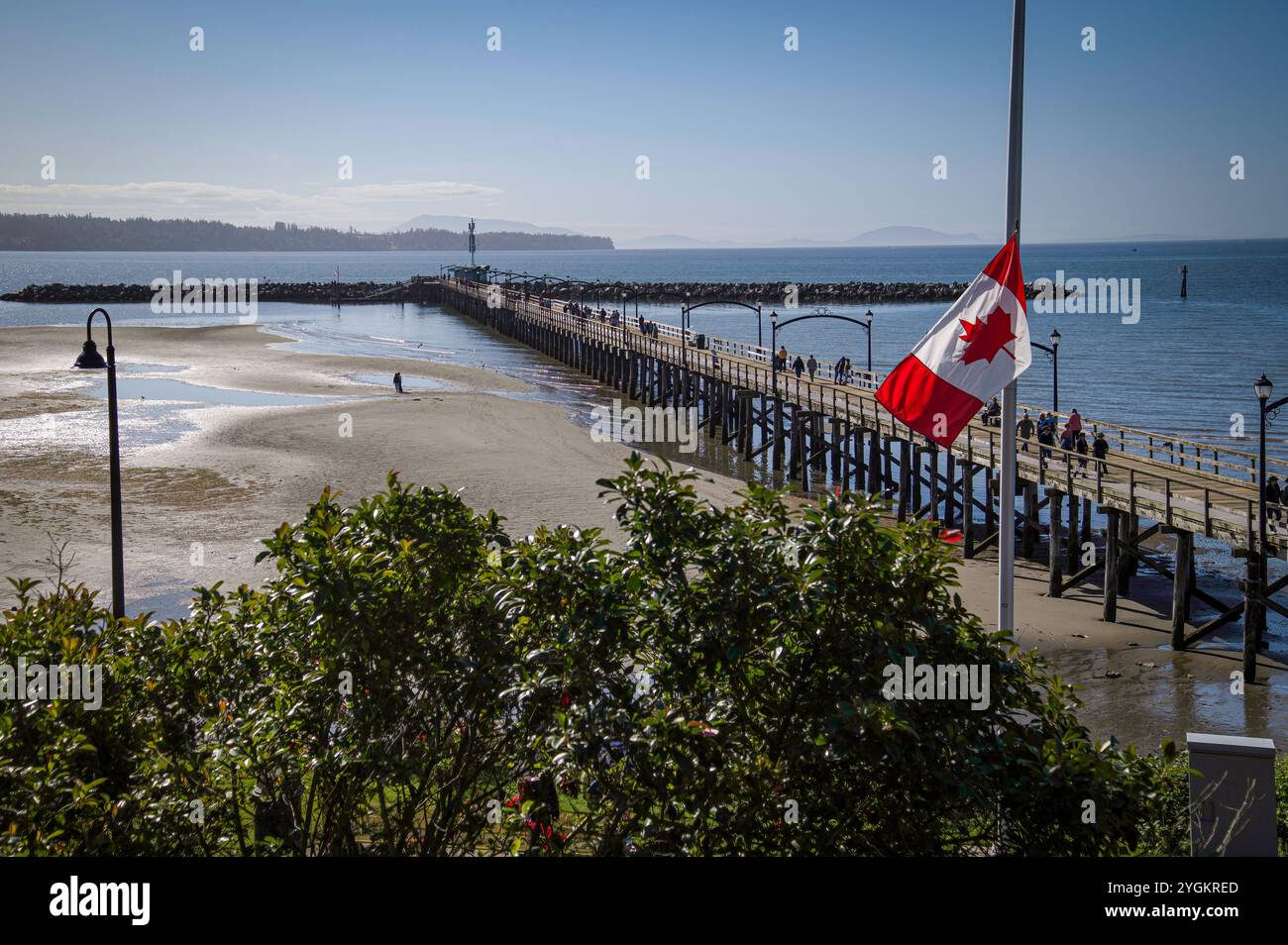 Foto der kanadischen Flagge und des 470 Meter langen, hölzernen White Rock Pier, der ursprünglich 1914 erbaut wurde und Kanadas längster Pier. Stockfoto