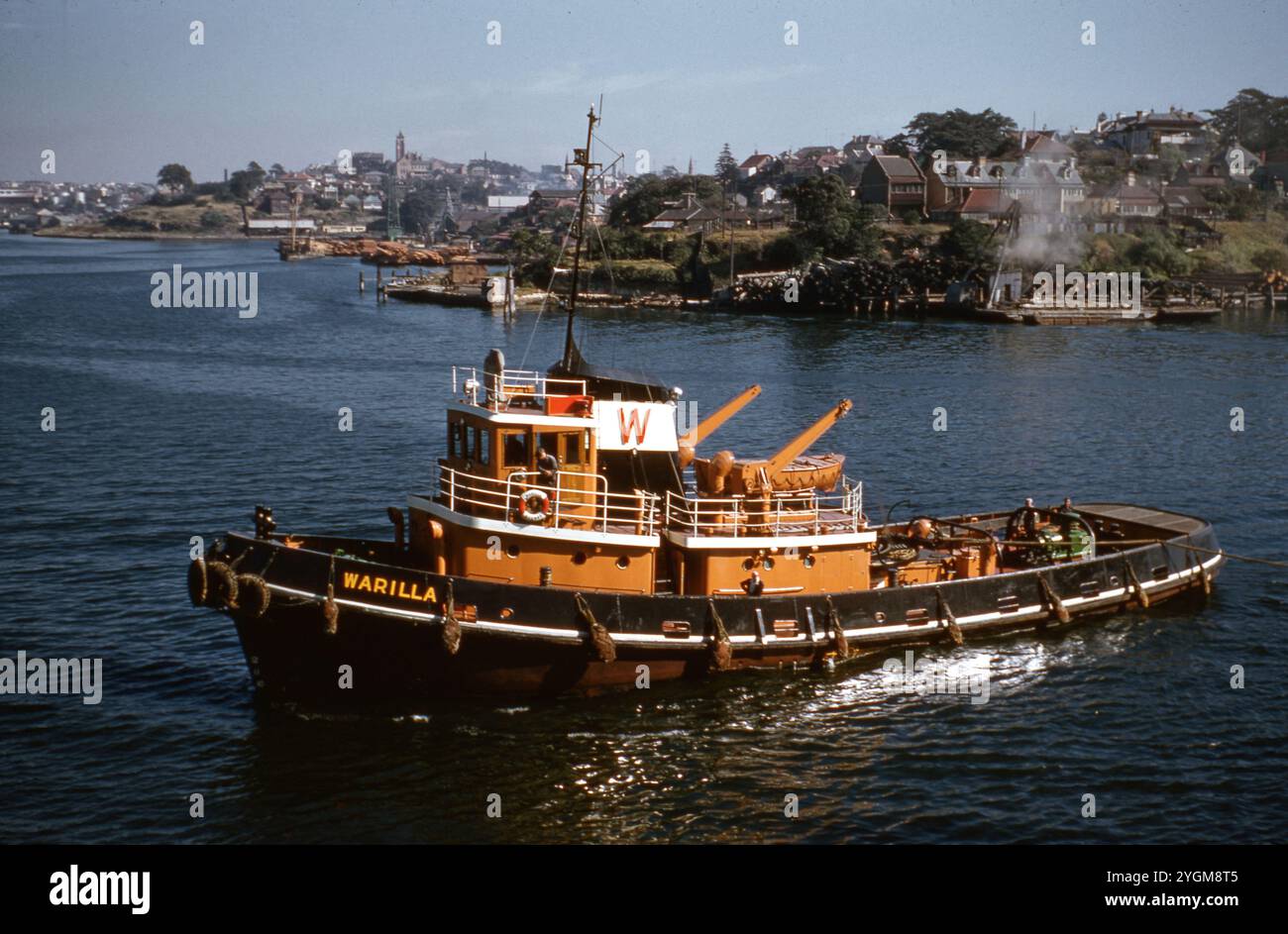 Forschungsschiff Warilla auf Küstengewässern der 1960er Jahre: Ein Farbfoto des Forschungsschiffes Warilla, das in den 1960er Jahren in Küstengewässern unterwegs war Das Schiff, das in einem auffälligen orange-schwarzen Farbschema mit seinem Namen deutlich sichtbar ist, ist mit nahe gelegenen Küstenlandschaften im Hintergrund zu sehen. Ursprünglich für Forschungszwecke genutzt, war die Warilla Teil des Seeverkehrs im Südpazifik und in den umliegenden Gebieten. Das Bild zeigt das einzigartige Design des Schiffes und die maritime Technologie der Epoche und bietet einen Einblick in historische Forschungsaktivitäten auf See. Stockfoto