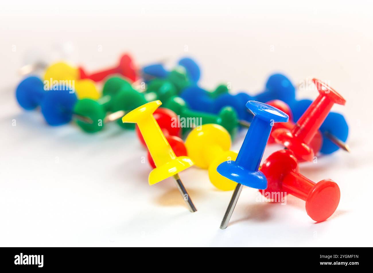 Eine Sammlung von mehrfarbigen Stecknadeln, die auf einer weißen Oberfläche verstreut sind und leuchtende Rot-, Blau-, Gelb- und Grüntöne zeigen Stockfoto