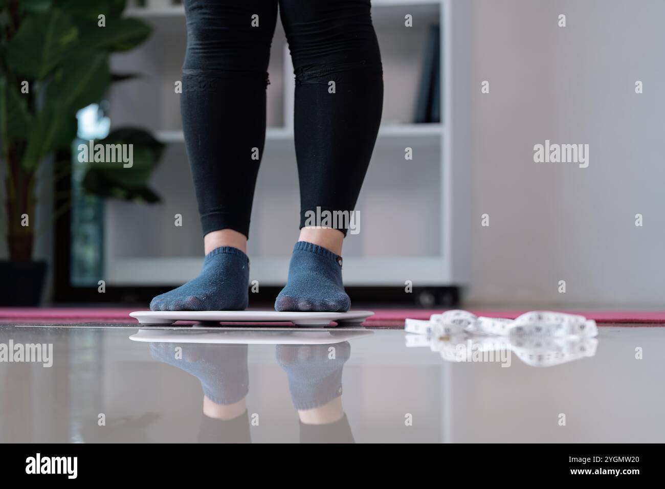 Frau, die auf der Waage mit Maßband steht, in modernem Home Setting, das Gewichtsmanagement und Gesundheitsbewusstsein hervorhebt Stockfoto