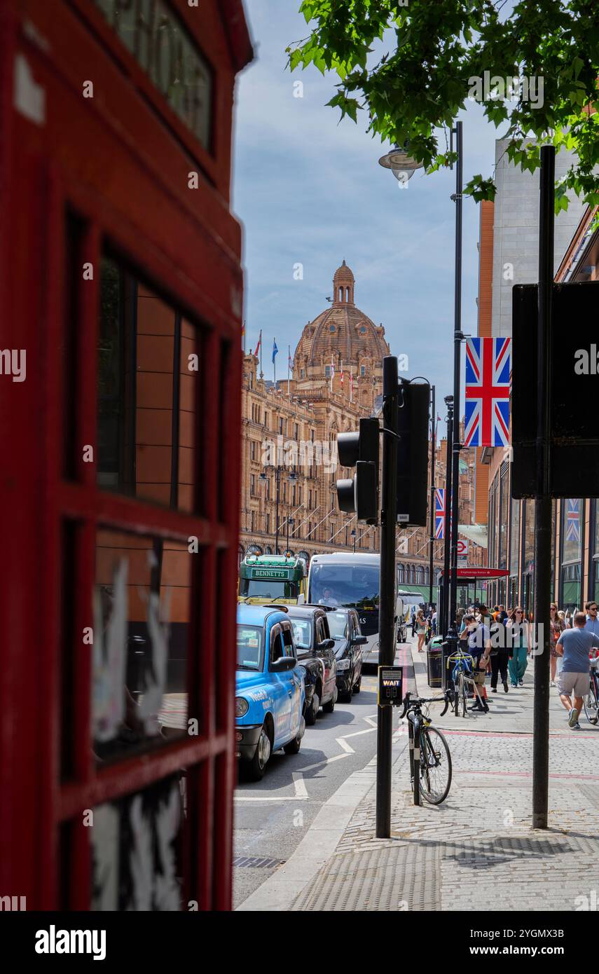 London - 06 16 2022: Blick auf die Brompton Rd mit einer verschwommenen roten Telefonbox im Vordergrund und Harrods Kaufhaus im Hintergrund Stockfoto