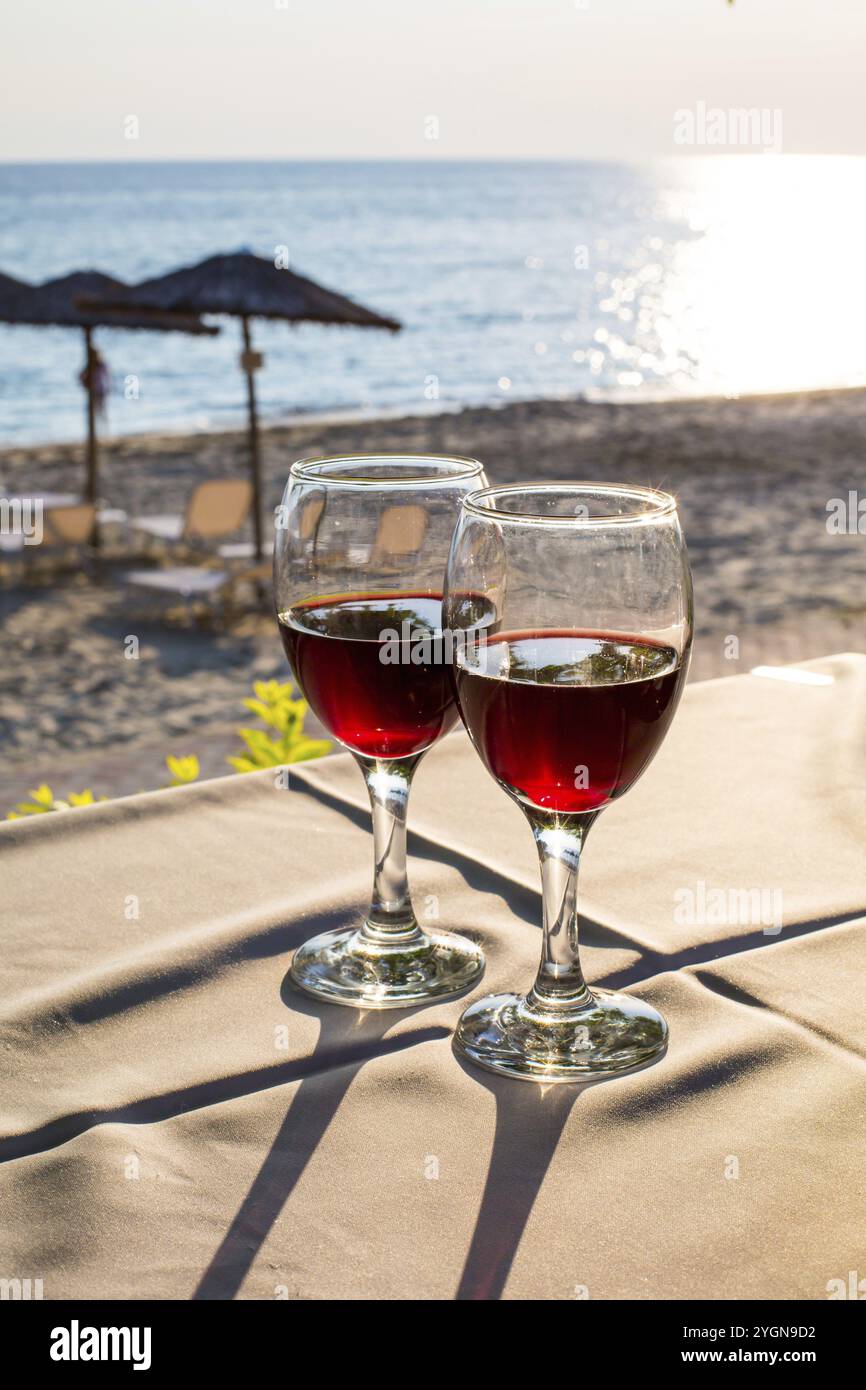 Zwei Gläser mit Rotwein, Meer mit Sonne Reflexion, Sonnenuntergang am Strand im Hintergrund. Sommer Urlaub Konzept Stockfoto