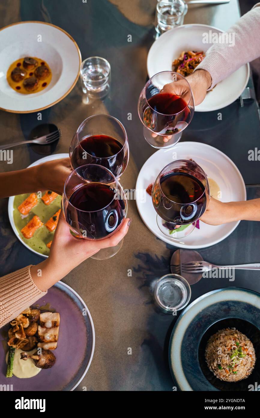 Freunde, die mit Rotwein bei einem modernen Fusionsküche-Dinner rösten, Blick von oben auf ein gemeinsames Dining-Erlebnis in einem gehobenen Restaurant Stockfoto