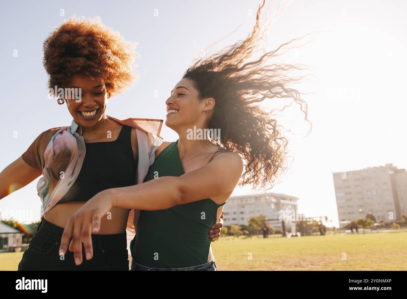 Zwei fröhliche Freunde genießen einen lustigen Moment im Stadtpark und feiern ihren unbeschwerten Lebensstil an einem sonnigen Tag. Stockfoto