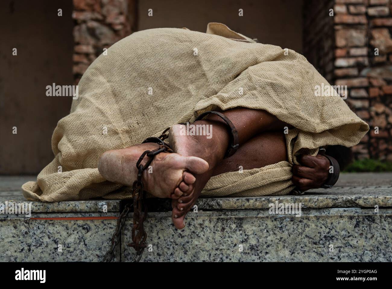 Schwarze Frau, verkleidet als Sklave in Ketten, liegt auf der Treppe einer Straße in Pelourinho. Sklaverei in Brasilien. Darstellung der Sklaven Anastacia. Stockfoto