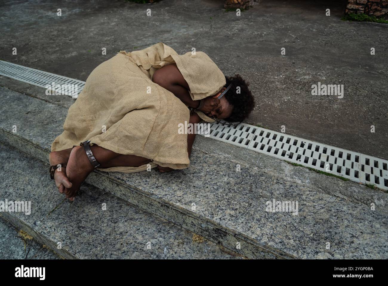 Schwarze Frau, verkleidet als Sklave in Ketten, liegt auf der Treppe einer Straße in Pelourinho. Sklaverei in Brasilien. Darstellung der Sklaven Anastacia. Stockfoto