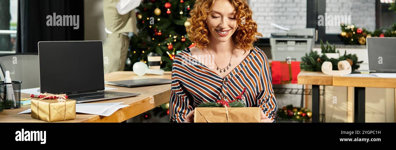 Schöne Frau mit Geschenk mit ihrem Kollegen, der Weihnachtsbaum im Hintergrund dekoriert. Stockfoto