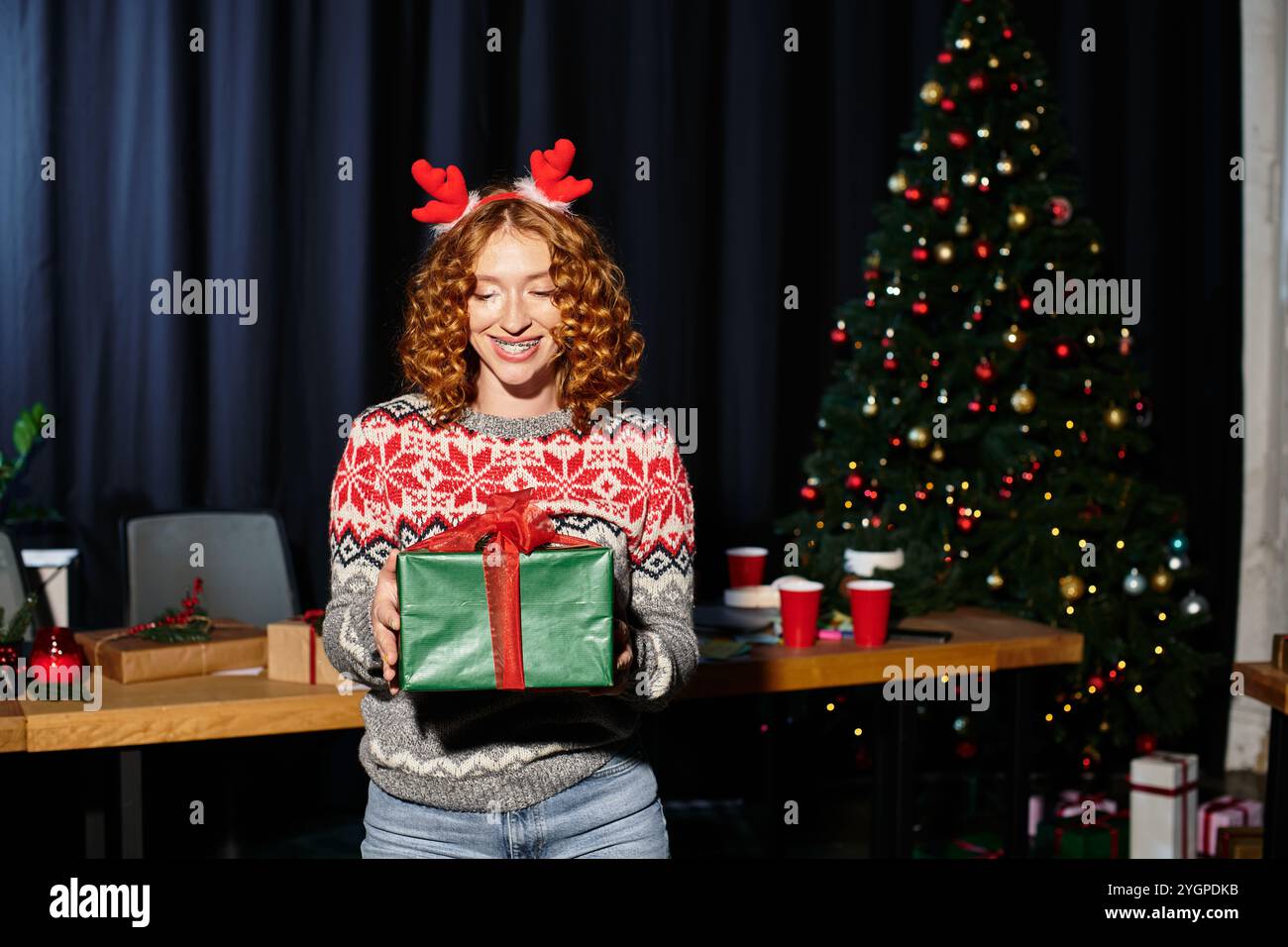 Junge Frau mit Geschenk in den Händen in festlichem Pullover im Büro. Stockfoto