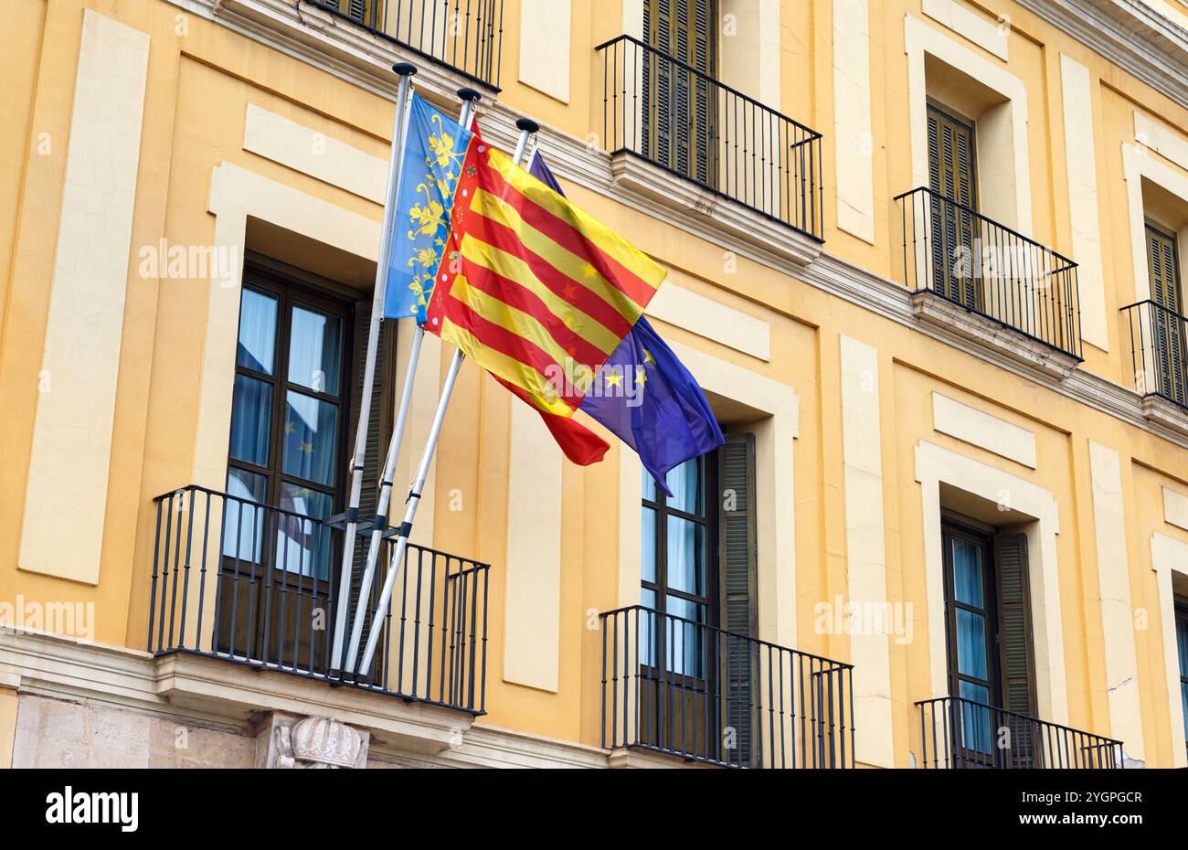 Farbenfrohe Fahnen wehen aus einem historischen Gebäude in Valencia und zeigen regionalen Stolz und Einheit unter klarem Himmel. Stockfoto