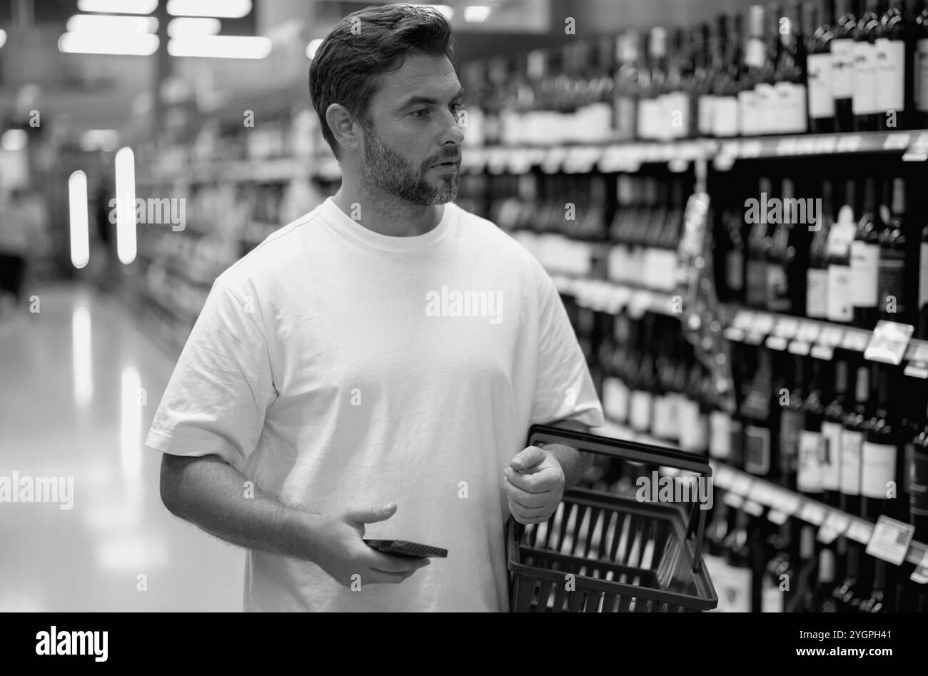 Ein Mann, der Alkoholflaschen im Schnapsladen aussucht. Ein Mann, der Produkte im Supermarkt kauft. Supermarkt und Supermarkt. Rabatt, Verkaufskonzept. Stockfoto