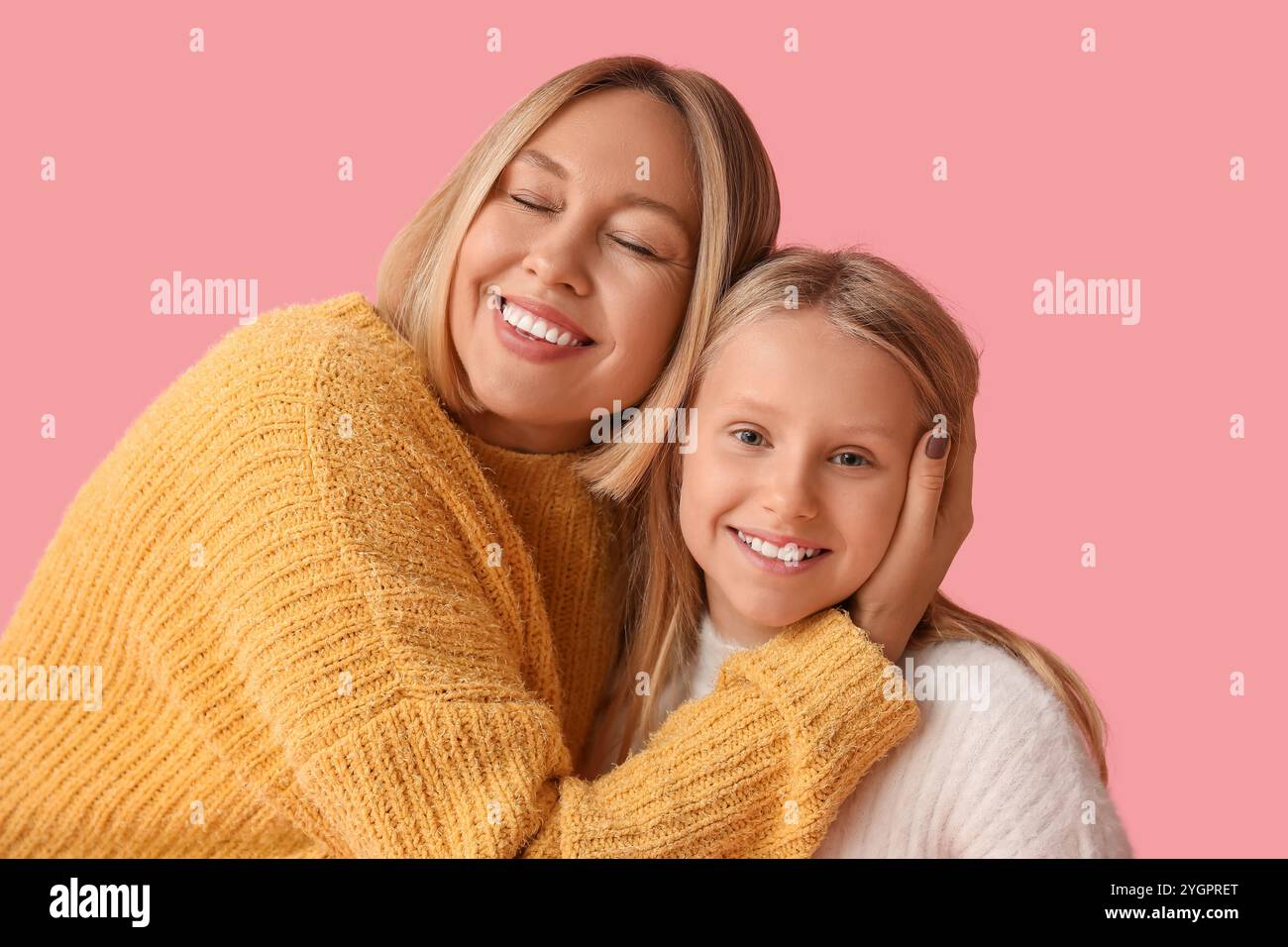 Schöne Frau und ihre süße Tochter in stylischen Pullis auf rosa Hintergrund Stockfoto