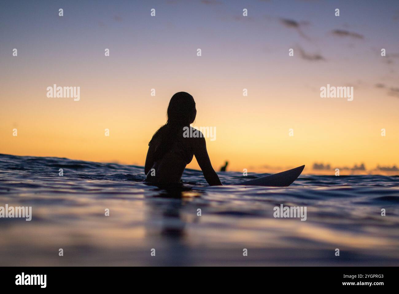 Eine ruhige Szene bei Sonnenuntergang mit einem Surfer auf ruhigen Gewässern in Queens, Waikiki Stockfoto