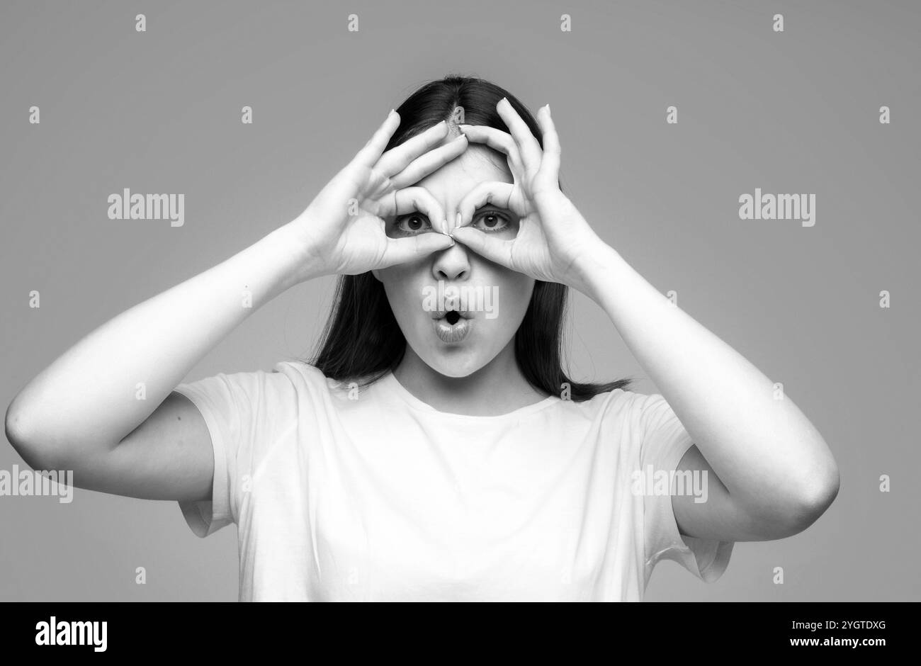 Lustige Frau mit Fingeraugen. Nahaufnahme eines wunderschönen weiblichen Models, das die Kamera durch die Finger betrachtet. Gesichtsausdrücke, Emotionen und Körper Stockfoto