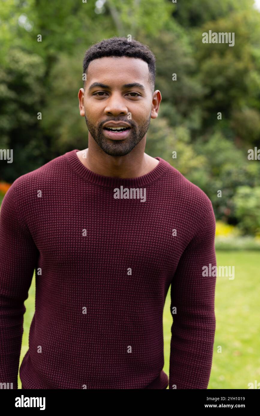 Lächelnder Mann in kastanienbraunem Pullover, der die Zeit draußen im Garten genießt Stockfoto