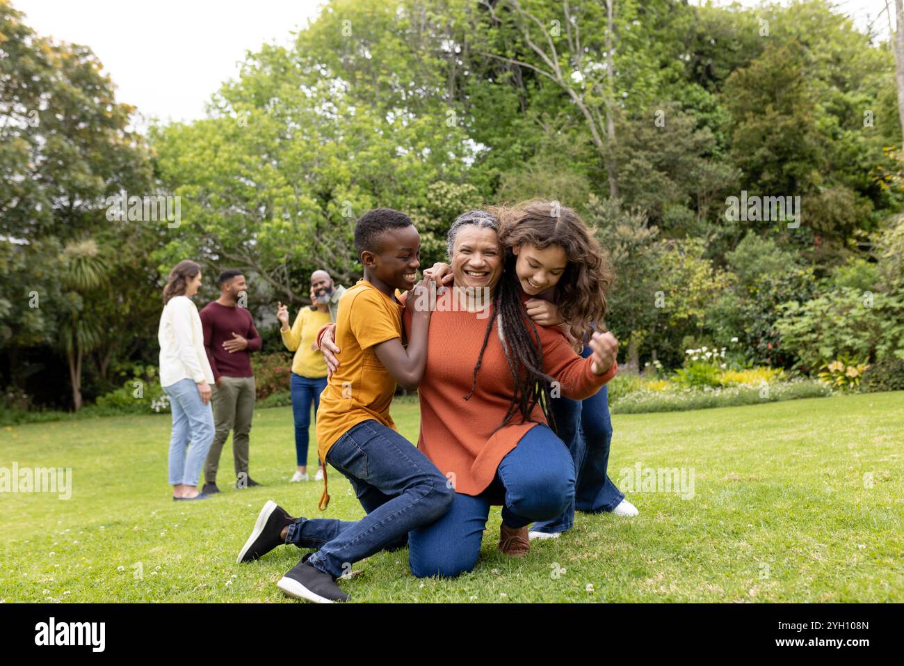 Die Familie, die gemeinsam verspielte Momente im sonnigen Garten genießt, lächelt und umgeht Stockfoto