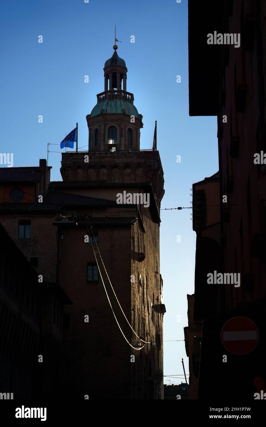Silhouette eines historischen Gebäudes mit Turm und Flagge vor einem klaren blauen Himmel in der Abenddämmerung in Bologna, Italien Stockfoto