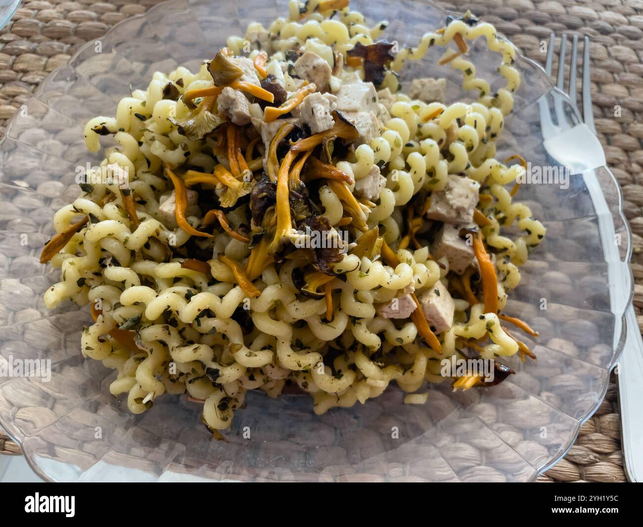 Gedrehte Nudeln mit Kräutern, gelben Fußpilzen und Tofu auf einem durchsichtigen Teller, veganes Gericht Stockfoto