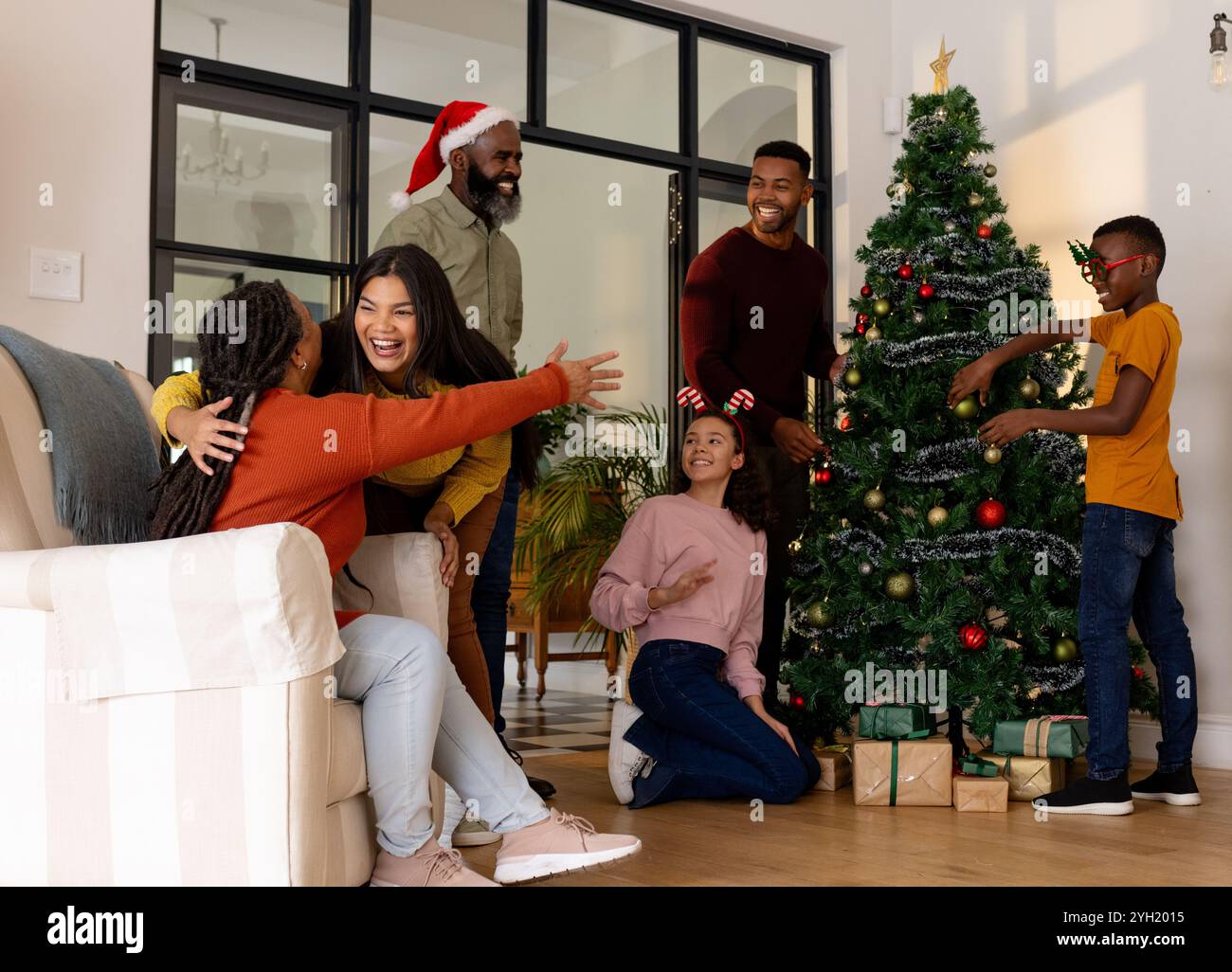 Multirassische Familie, die den Weihnachtsbaum zusammen dekoriert, Freude und Lachen zu Hause teilt Stockfoto