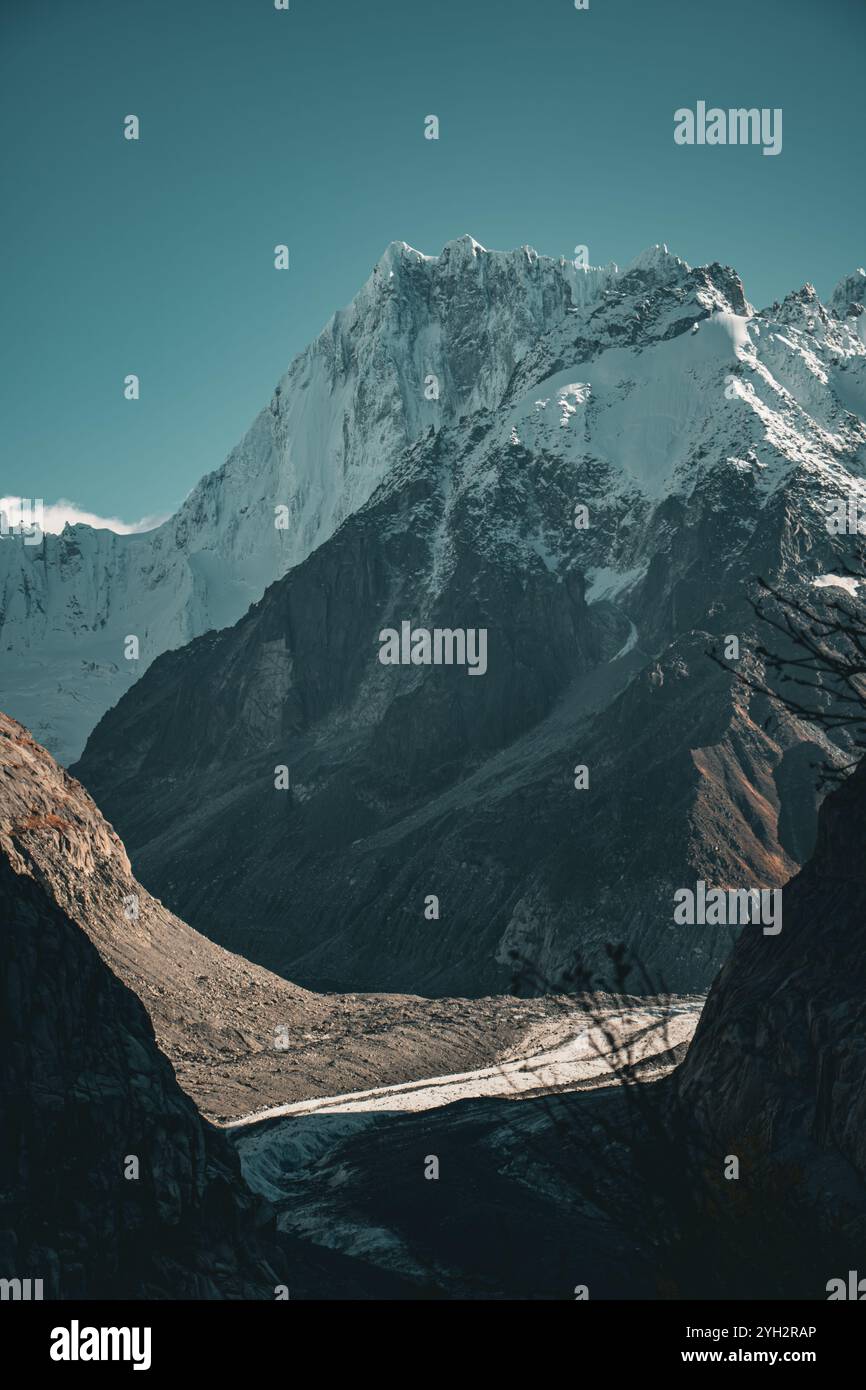 Majestätischer, schneebedeckter Gipfel, der sich über einem felsigen Tal erhebt, mit sanftem Sonnenlicht, das die zerklüftete Alpenlandschaft hervorhebt und Schatten über den Gletscher wirft. Stockfoto