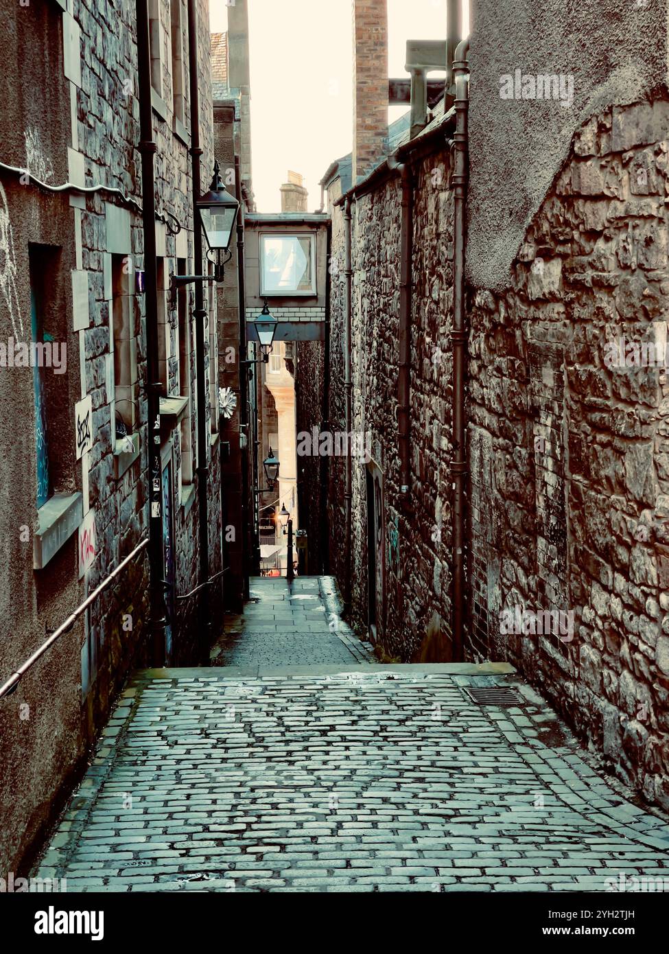 'Stimmungsvolle enge Gasse mit Steinmauern und Kopfsteinpflasterstraße, die nach unten durch alte Gebäude führt und einen Sinn für Geschichte weckt.' - Smartphone-aufgenommenes Stockfoto