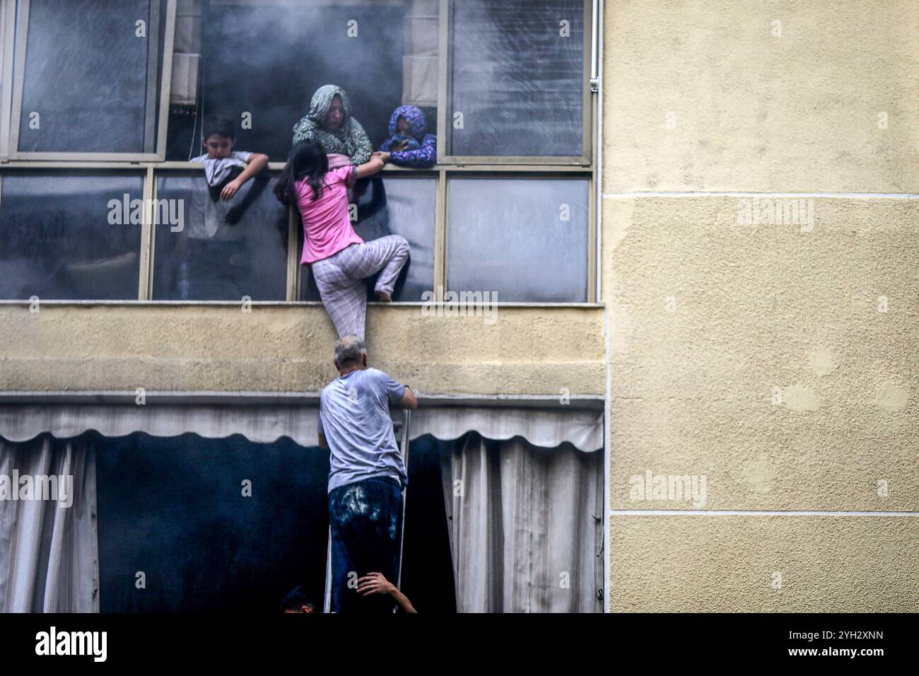 Beirut, Libanon. November 2024. Libanesische Zivilschutzbeamte retten eine Familie aus einem Gebäude, das Feuer fing, nachdem eine Generatorexplosion auf einem Parkplatz Flammen auf benachbarte Gebäude im Bezirk Hamra in Beirut ausbreitete. Das libanesische Innenministerium berichtete, dass 16 Menschen an starkem Rauch erstickten, 30 Autos entkernt wurden und mindestens drei Gebäude in Brand gerieten. Eine Person erlitt Verletzungen, nachdem sie vom Balkon gesprungen war, als sie versuchte, der Flamme zu entkommen. Marwan Naamani/dpa/Alamy Live News Stockfoto