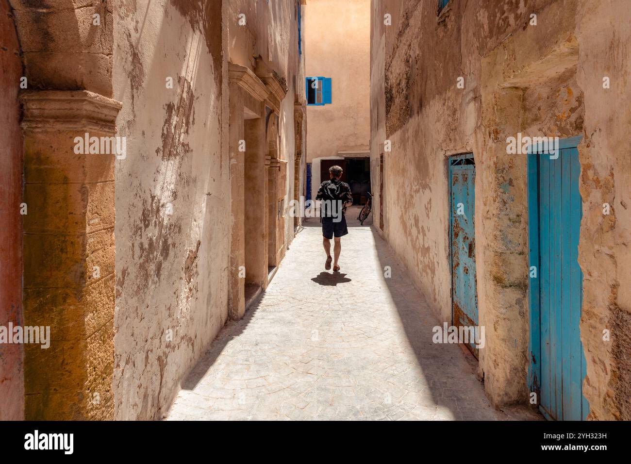 Eine Person, junger Erwachsener männlich, Besichtigungstour durch eine enge Gasse in Medina Essaouira, Marokko, Gebäude mit blau lackierten Türen Stockfoto