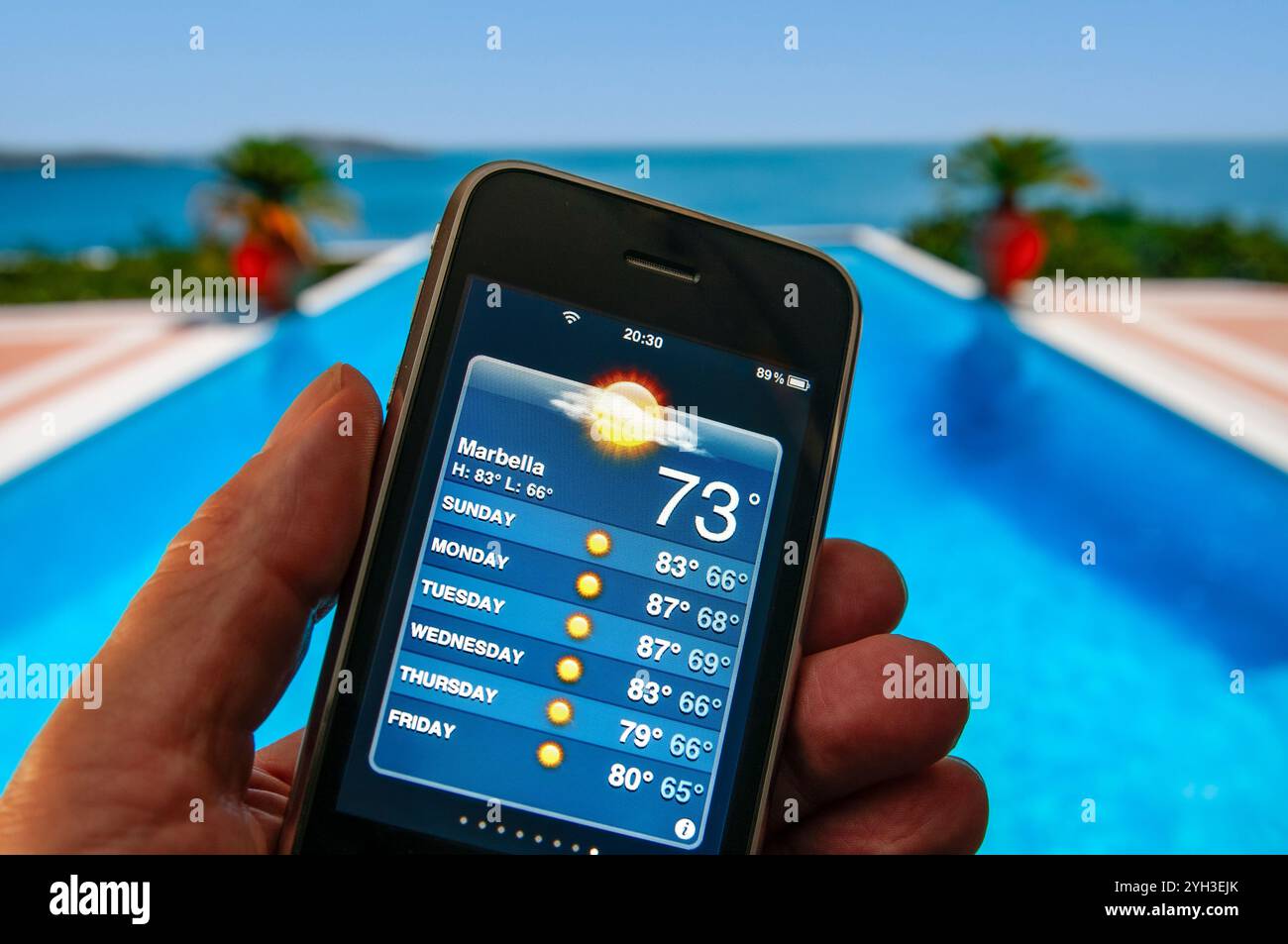 SPANIEN WETTER APP Hand hält Smartphone zeigt Woche von Marbella Urlaub Sonne auf Wetter Smartphone App Pool Einstellung Marbella Spanien Stockfoto