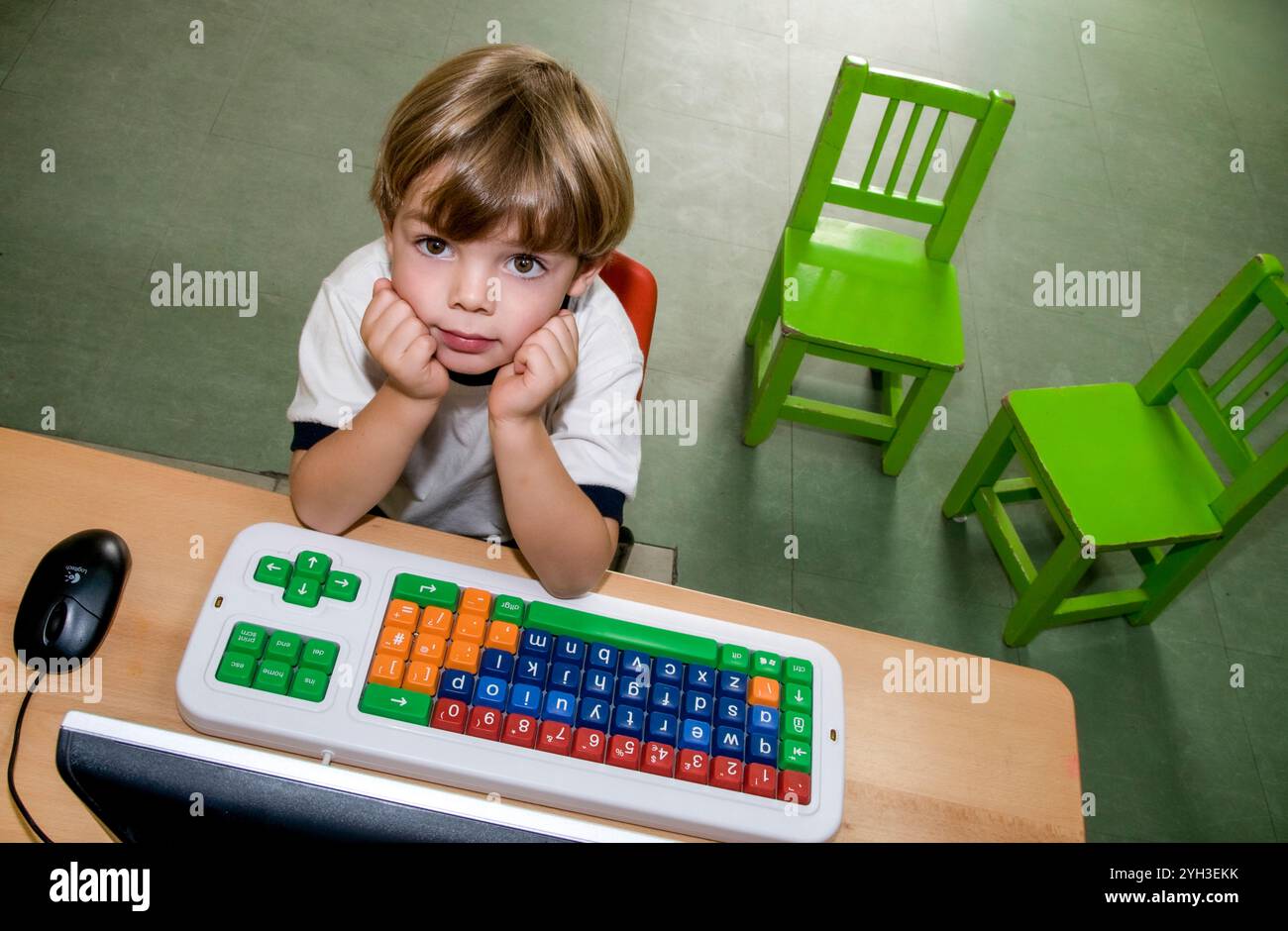 Computer & Kleinkind blonder Junge 4 Jahre Kindergarten Grundschule blickt von seinem Lerncomputer, seiner Maus und Tastatur nach oben Stockfoto