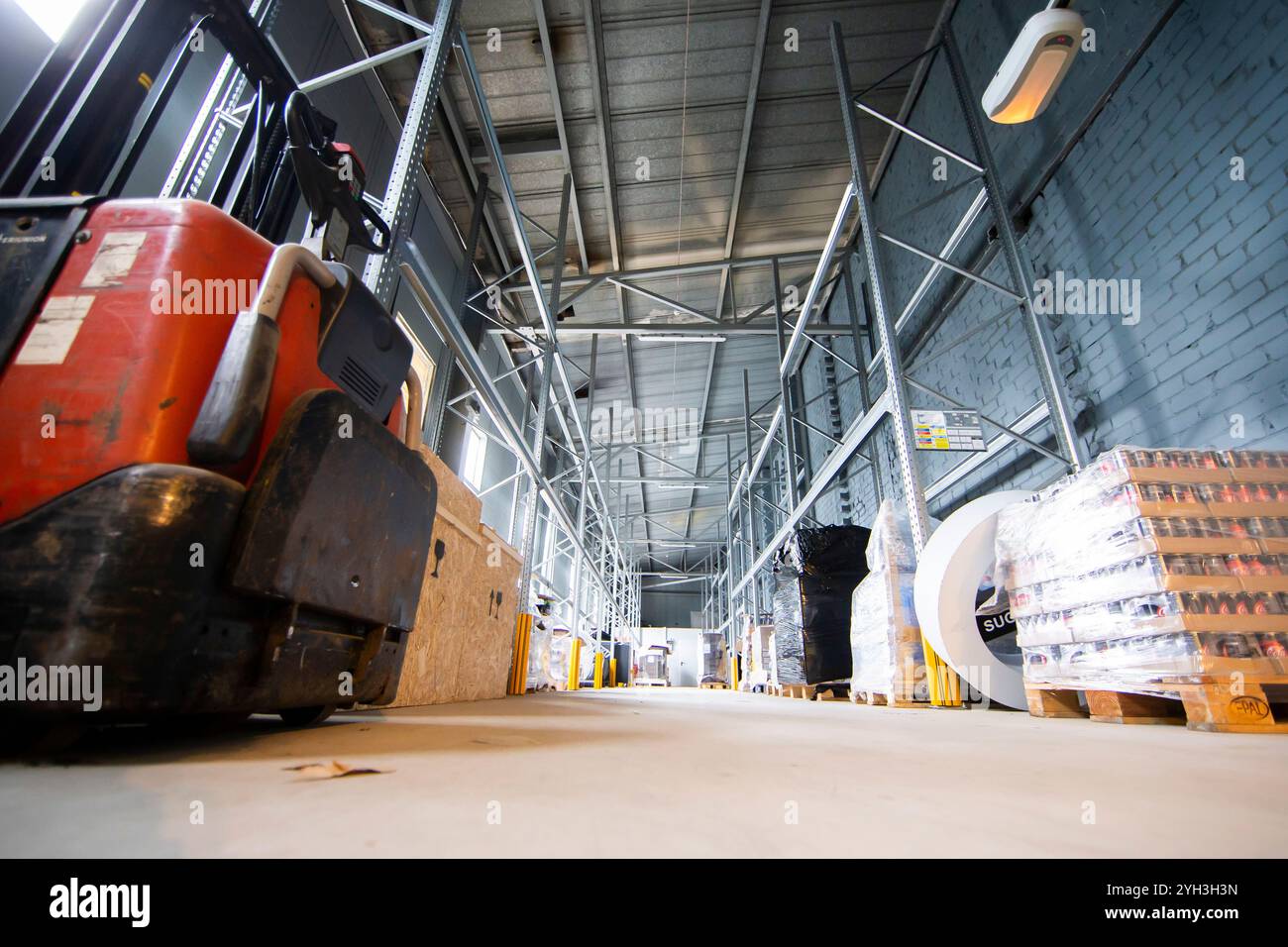 Innenraum des Lagers mit Industrieregeln, Paletten und einem roten Gabelstapler in Betrieb. Stockfoto