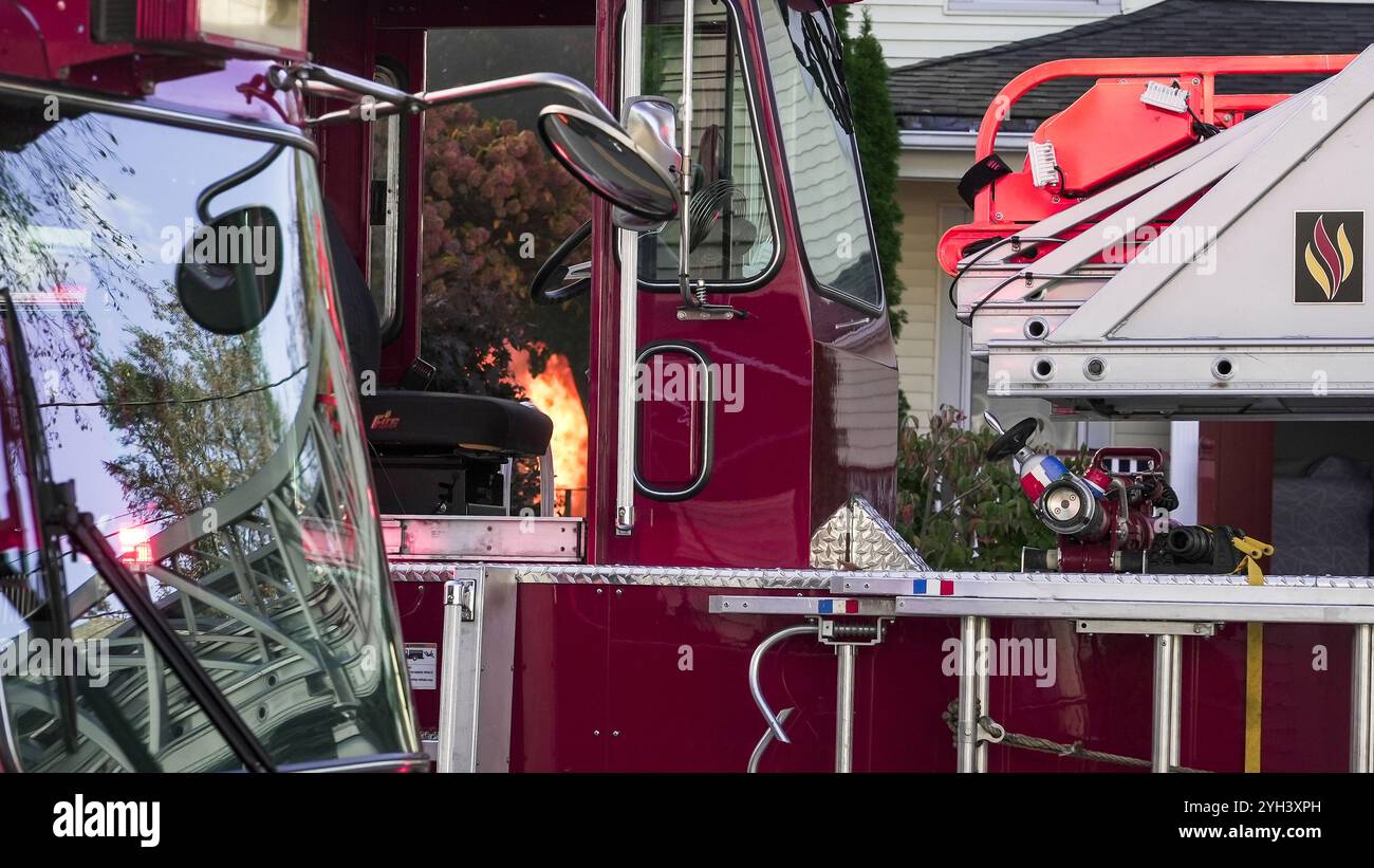 NORWALK, CT, USA – 1. NOVEMBER 2024: Ein Feuerwehrauto steht vor einem Haus, in dem Flammen in der offenen Kabinentür sichtbar sind. Stockfoto