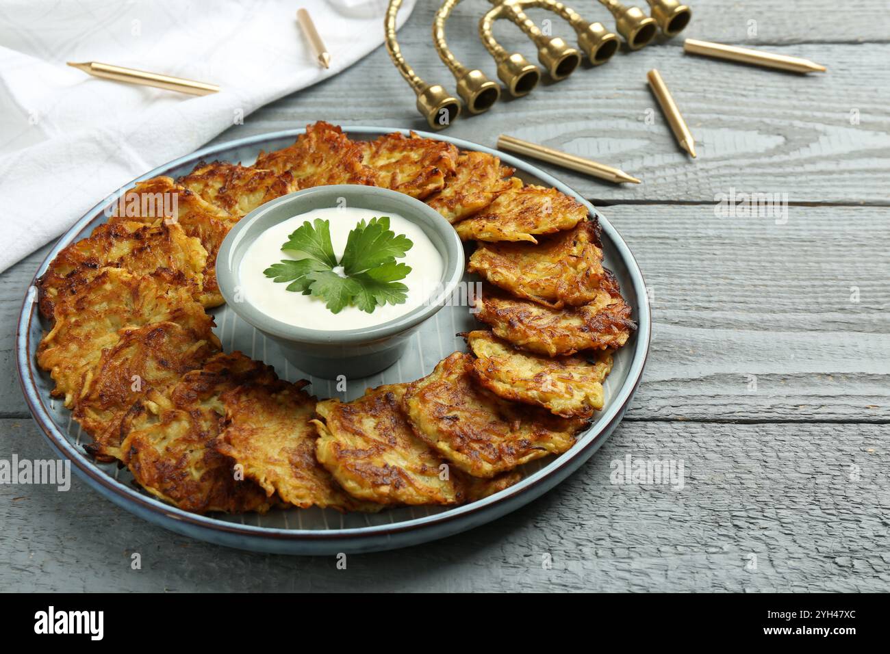 Leckere Kartoffelpfannkuchen, Menora und Kerzen auf grauem Holztisch, Nahaufnahme. Hanukkah festliches Essen Stockfoto