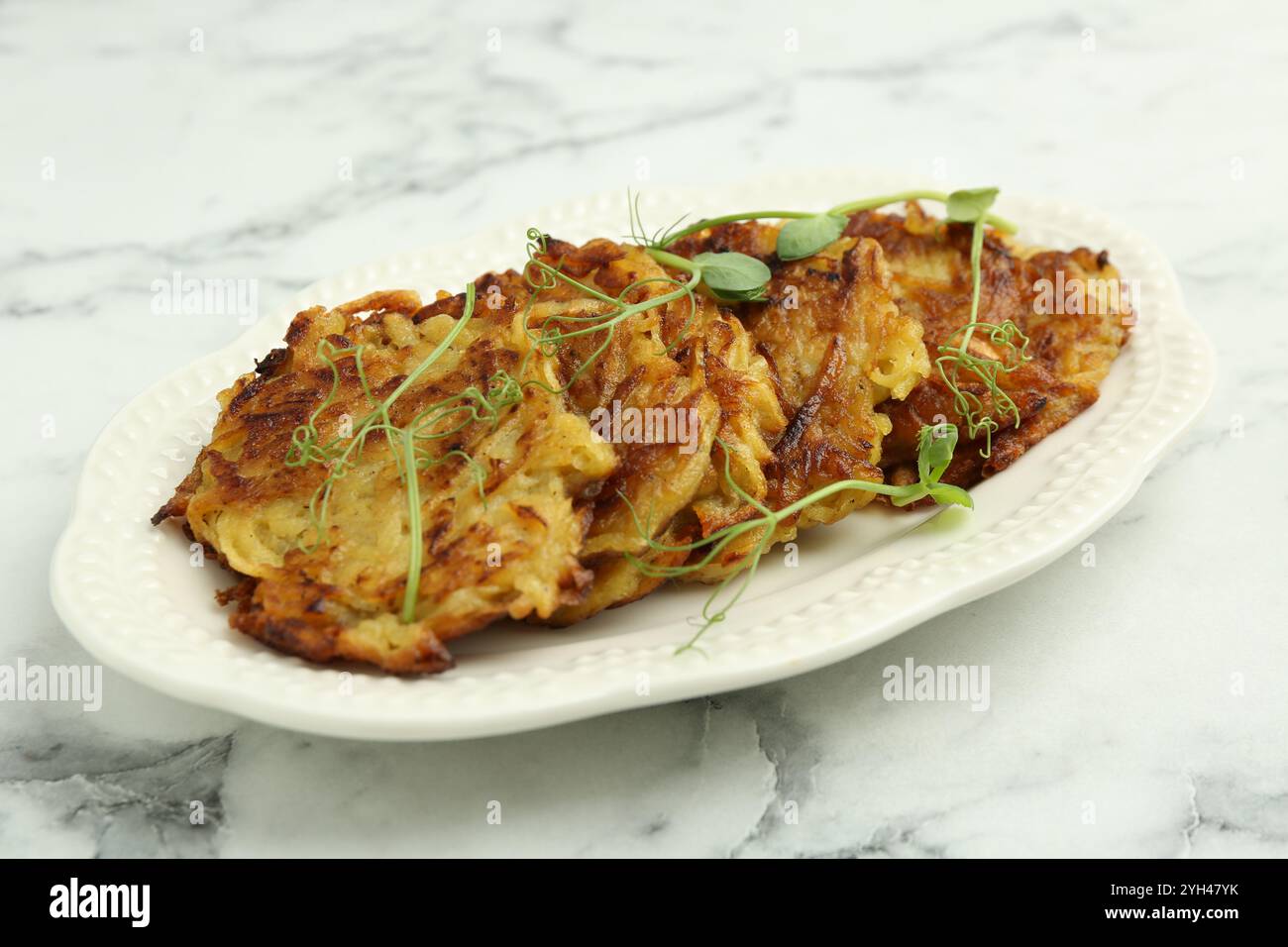 Köstliche Kartoffelpfannkuchen mit Mikrogrün auf weißem Marmortisch, Nahaufnahme Stockfoto