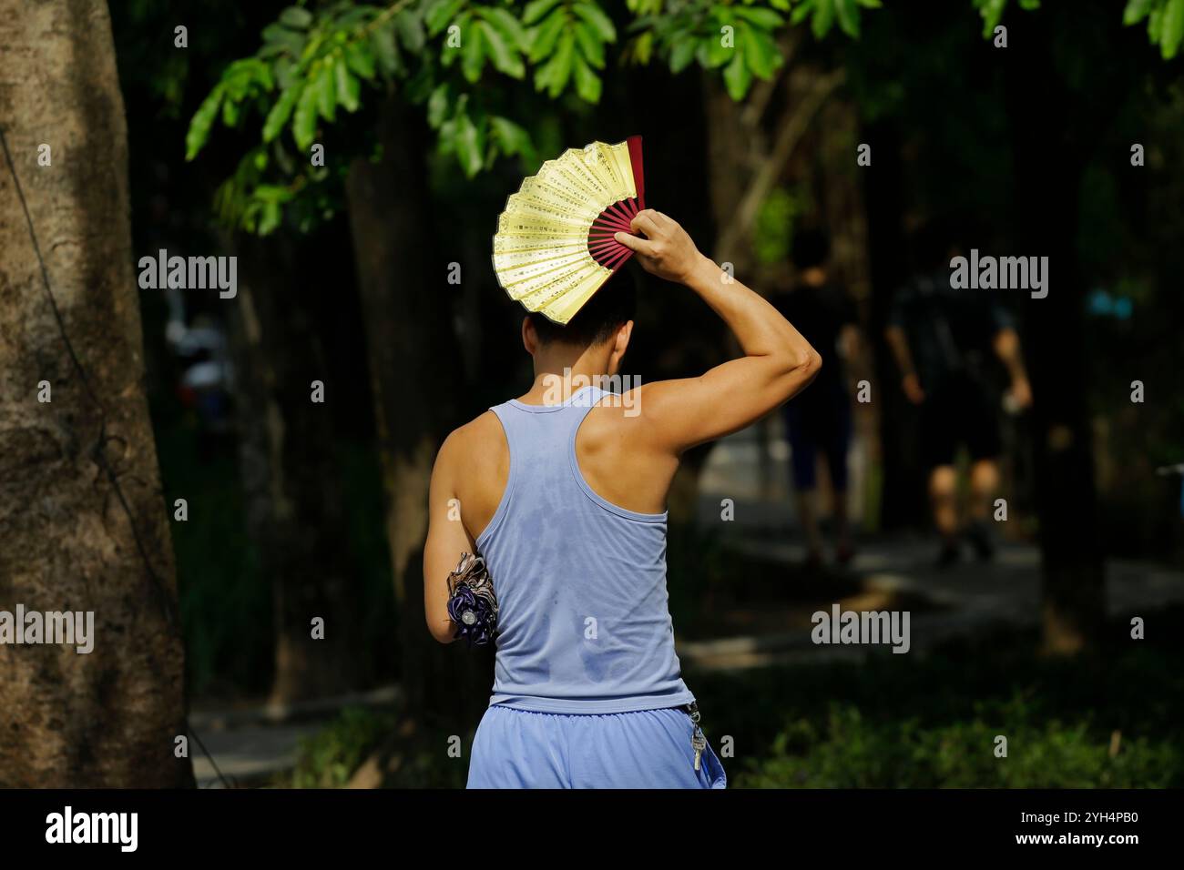 Hanoi, Vietnam - 10. Juli 2023: Man benutzt einen Ventilator, um sich vor der extrem heißen Sonne zu schützen, während man in der vietnamesischen Hauptstadt draußen spaziert. Stockfoto
