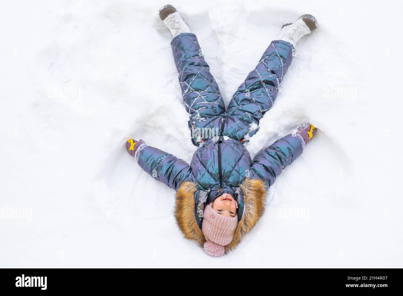 Ein Mädchen in einem blauen Jumpsuit macht Schneeengel im Schnee. Winterspaß, Spiele im Freien, Weihnachten Stockfoto