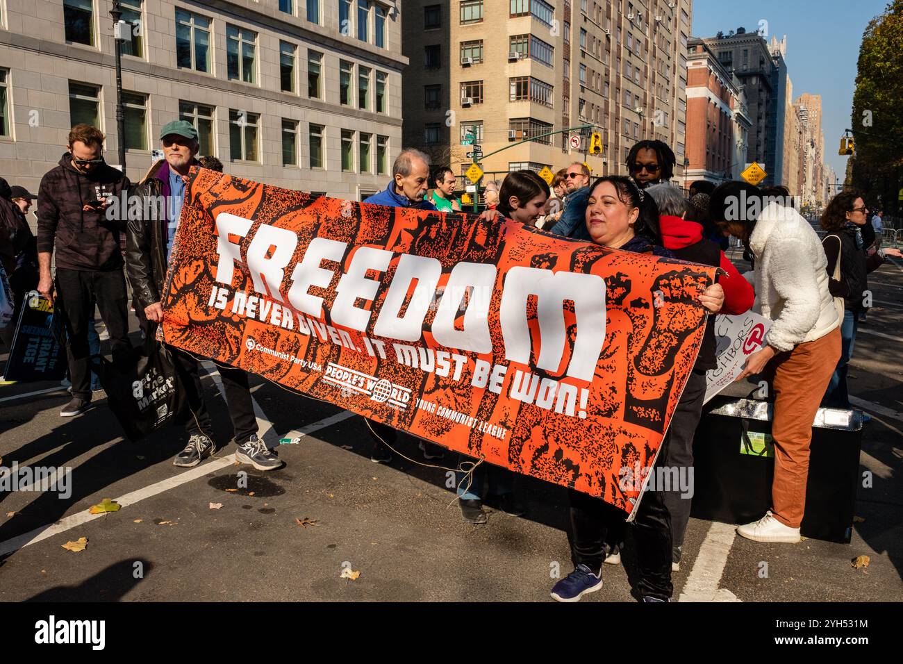 New York, NY, USA. November 2024. Demonstranten aus verschiedenen Gruppen und Einzelpersonen beteiligen sich an der protestmarsch „unsere Zukunft schützen“ in der Nähe des Kolumbus Circle, um gegen die von der neuen Trump-Regierung vorgeschlagene Politik zu protestieren. Die Demonstranten der Jungen Kommunistischen Liga tragen ein Banner. Quelle: Ed Lefkowicz/Alamy Live News Stockfoto