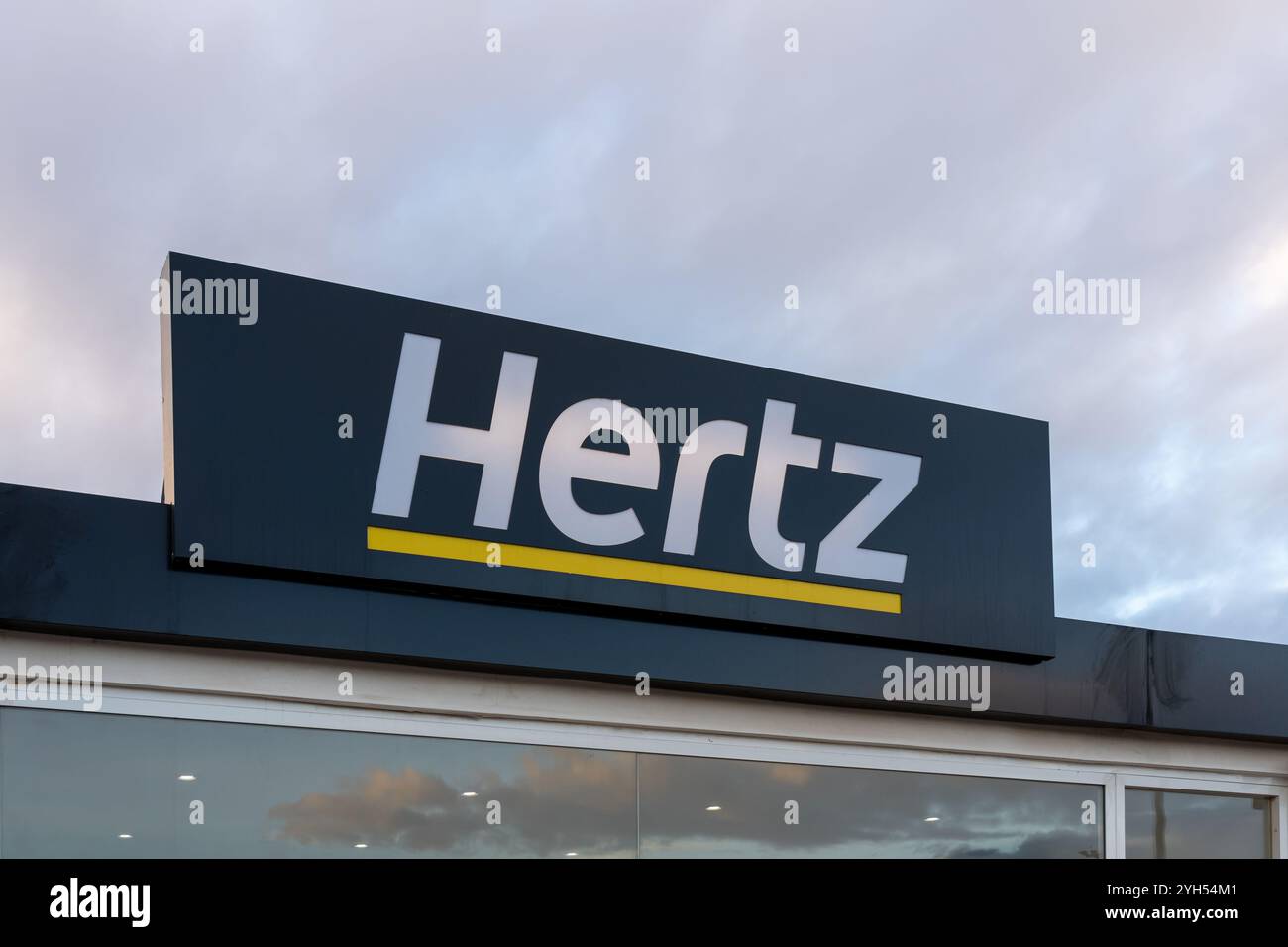 Nahaufnahme des Hertz-Logoschildes am Gebäude, das am frühen Morgen in der Autovermietung am Flughafen zu sehen ist Stockfoto