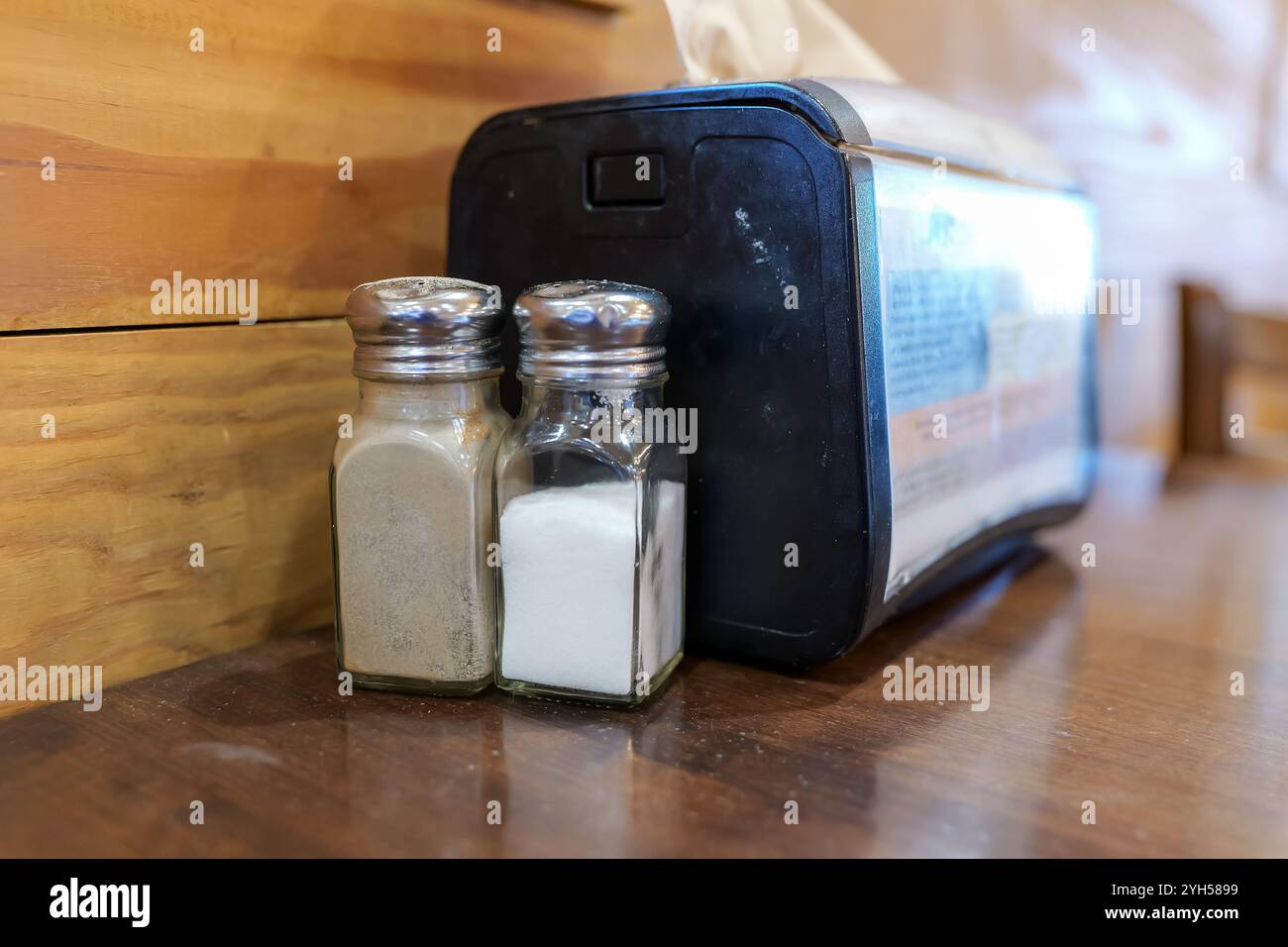 Salz- und Pfefferstreuer neben einem Serviettenspender auf einem hölzernen Kaffeetisch. Stockfoto
