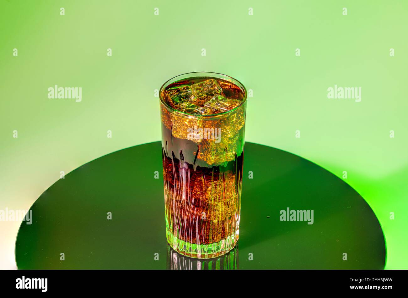 Glas Limonade mit Eiswürfeln auf reflektierender Oberfläche, beleuchtet von grünem Hintergrund für einen lebendigen visuellen Effekt. Stockfoto