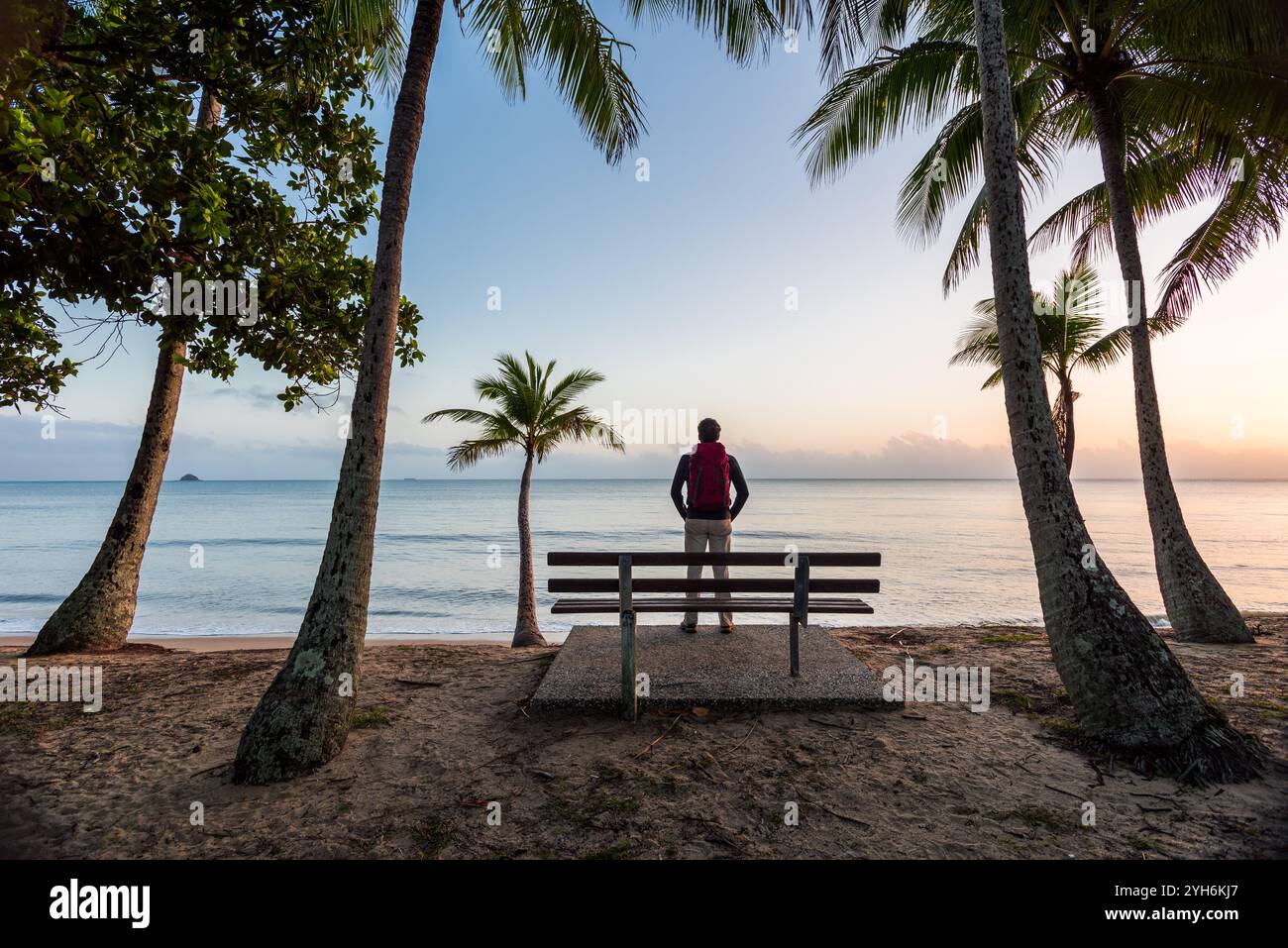 Mit Blick auf den Pazifik wird ein Rucksacktouristen an einem Strand von tropischen Kokospalmen eingerahmt, während er die frühen Sonnenaufgänge genießt. Stockfoto