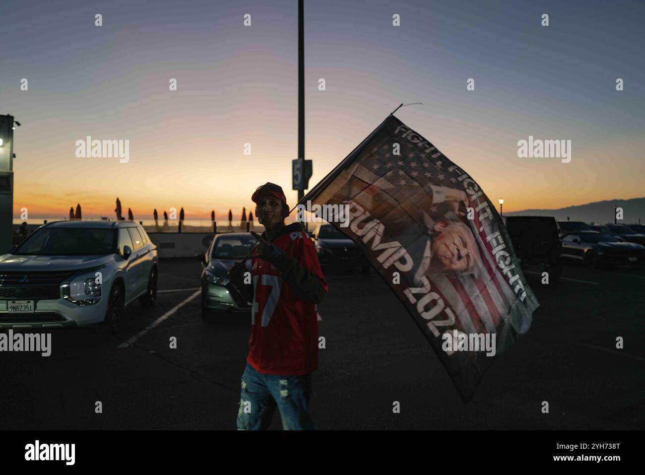 Santa Monica Beach, Kalifornien, USA. November 2024. Eine große, begeisterte Menge Trump-Anhänger versammelt sich bei Sonnenuntergang am Santa Monica Beach, schwenkt amerikanische Fahnen und jubelt die Wahlergebnisse. Der Himmel ist mit warmen Orange- und Rosa-Tönen bemalt, was das festliche Ambiente unterstreicht. In Santa Monica Beach feierten Trump-Anhänger seinen Sieg bei den US-Präsidentschaftswahlen 2024. Das Ereignis zog eine begeisterte Menge an, als die Leute Fahnen schwenkten, Slogans sangen und die Aufregung teilten. Quelle: SOPA Images Limited/Alamy Live News Stockfoto