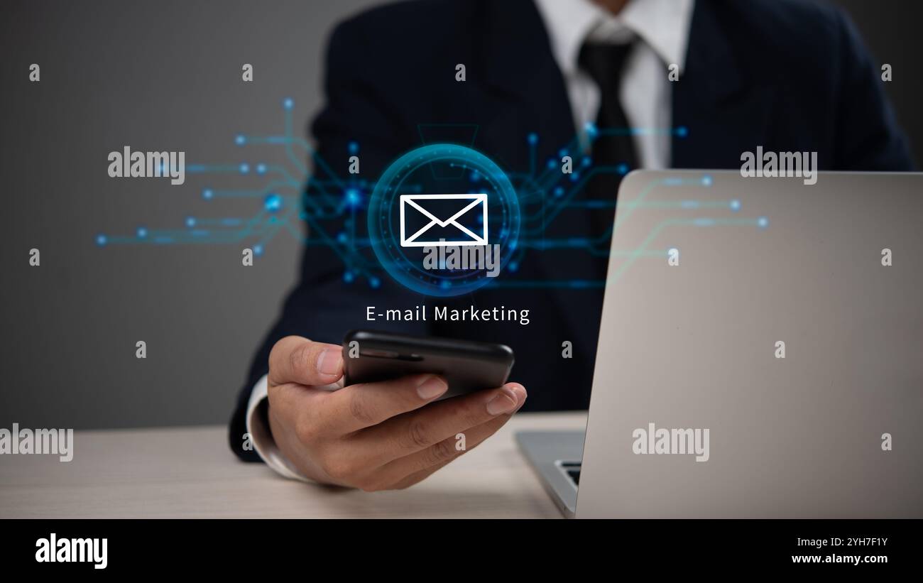 Geschäftsmann im Anzug, der ein Smartphone für E-Mail-Marketing verwendet, mit digitalen Grafiken, die Kommunikation und Technologie darstellen. Stockfoto