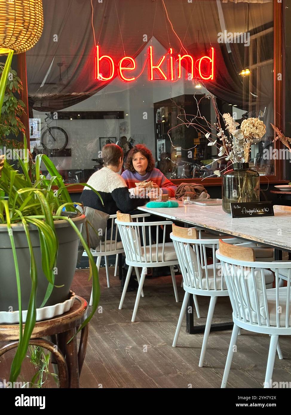 Eine Szene im beliebten Café/Restaurant A.. Horn in Kreuzberg, Berlin, Deutschland, ein Neonschild mit der Aufschrift „Be Kind“ im Hintergrund Stockfoto