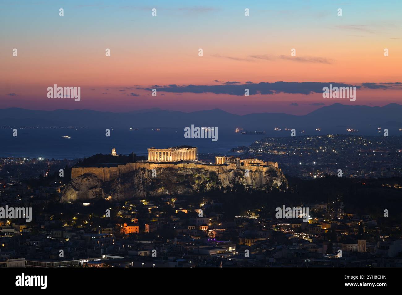 Blick auf die Stadt Athen und den Akropolis-Hügel mit dem Parthenon-Tempel, der bei Sonnenuntergang über dem Saronischen Golf beleuchtet wird. Athen, Griechenland Stockfoto