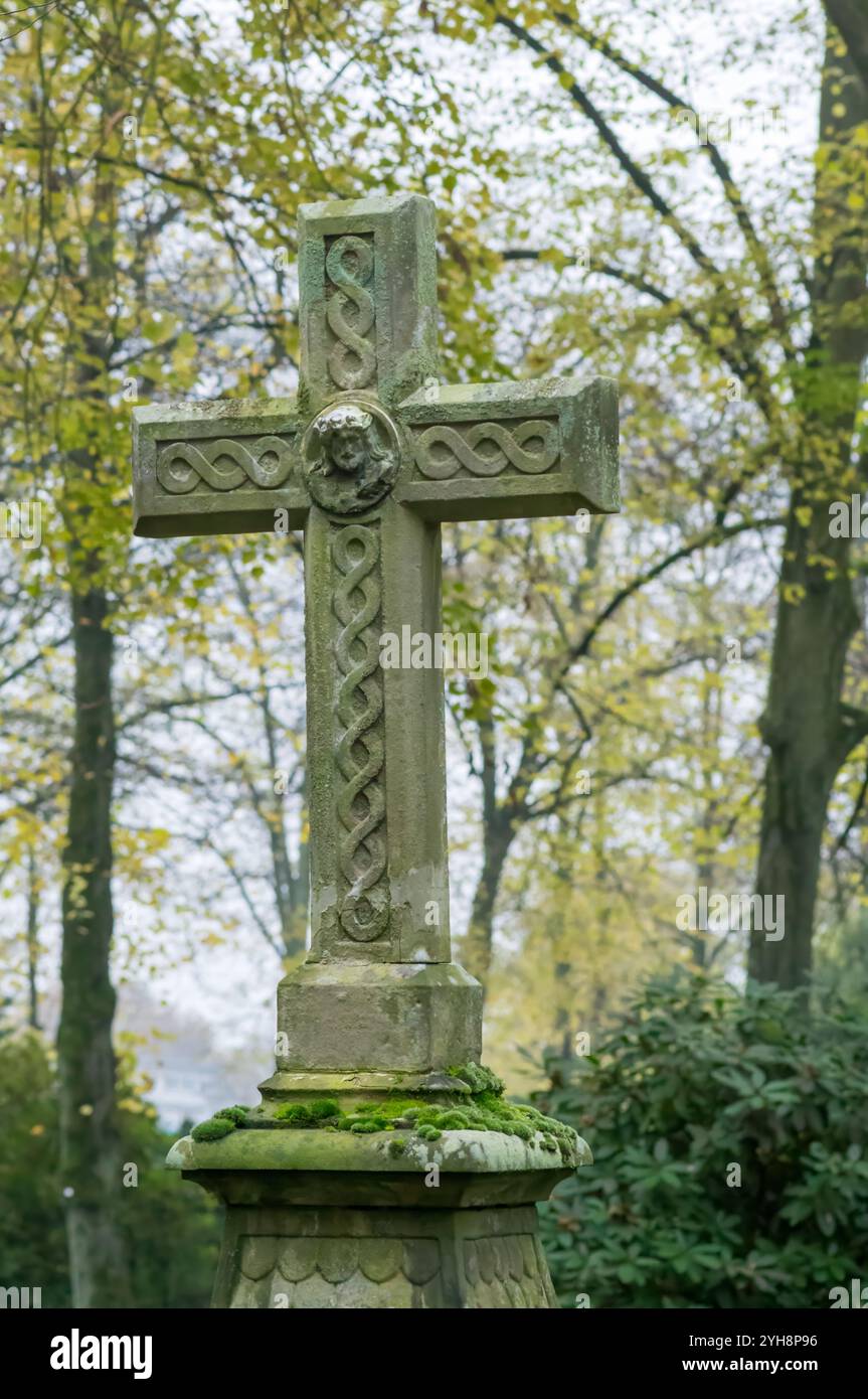 Verwittertes Steinkreuz mit keltischen Knoten und einem Gesicht jesu, feierlich auf einem ruhigen Friedhof stehend, symbolisiert Glauben, Erinnerung und et Stockfoto